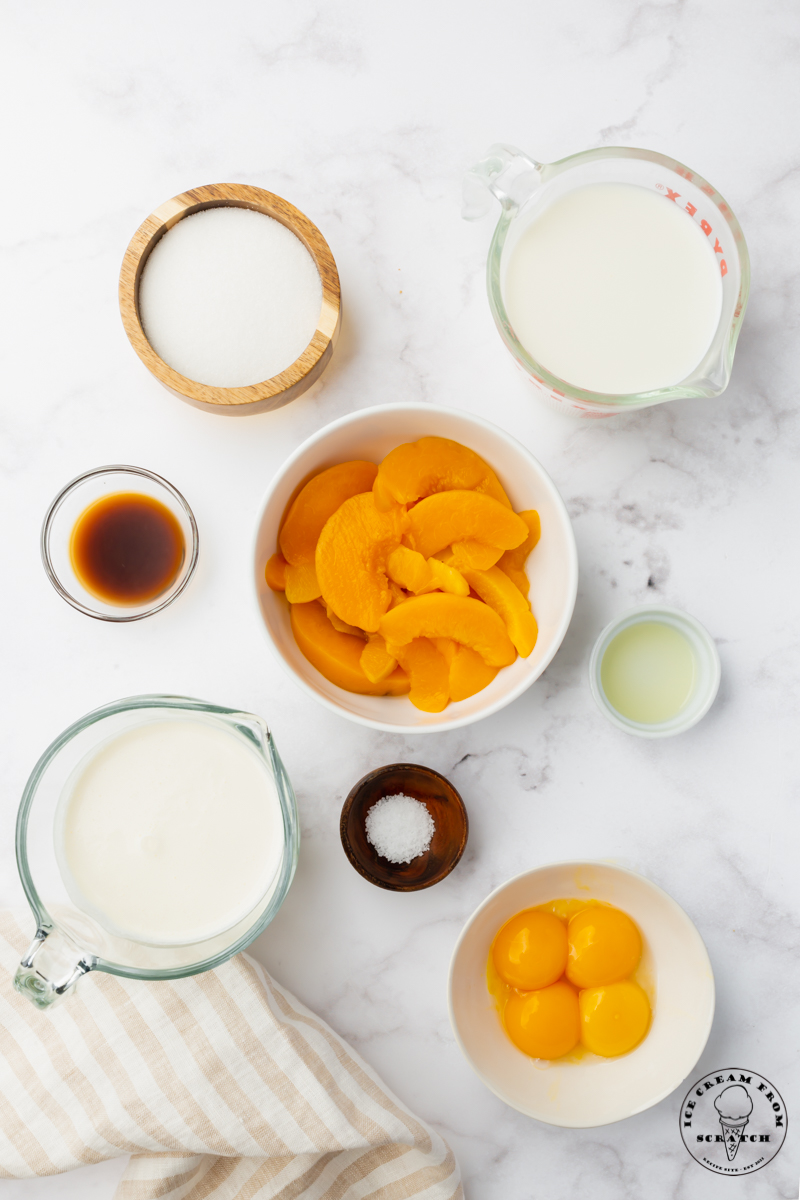The ingredients for making peach ice cream all measured into separate bowls at set on a marble countertop. Viewed from above.