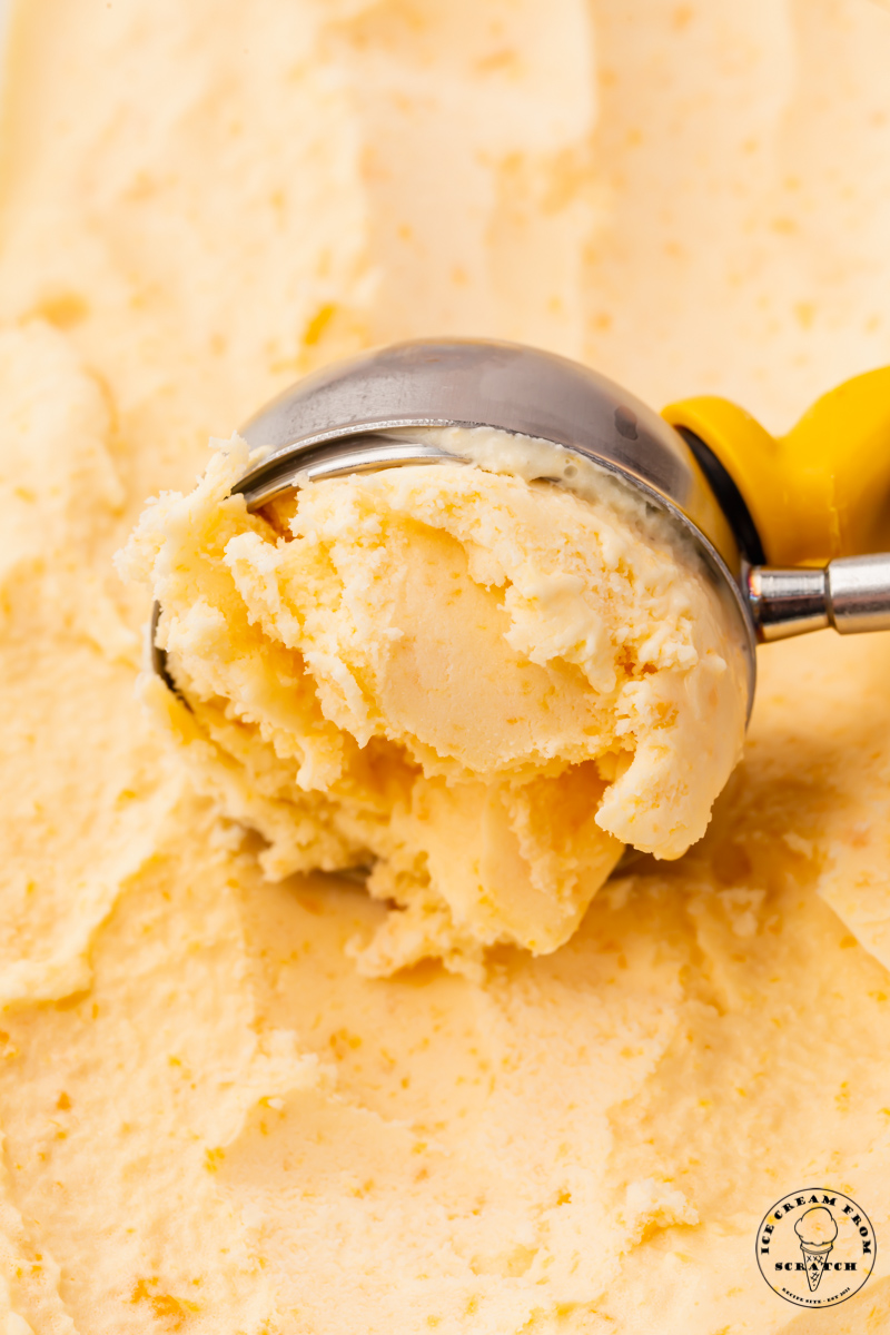 homemade peach ice cream being scooped with a metal ice cream scoop