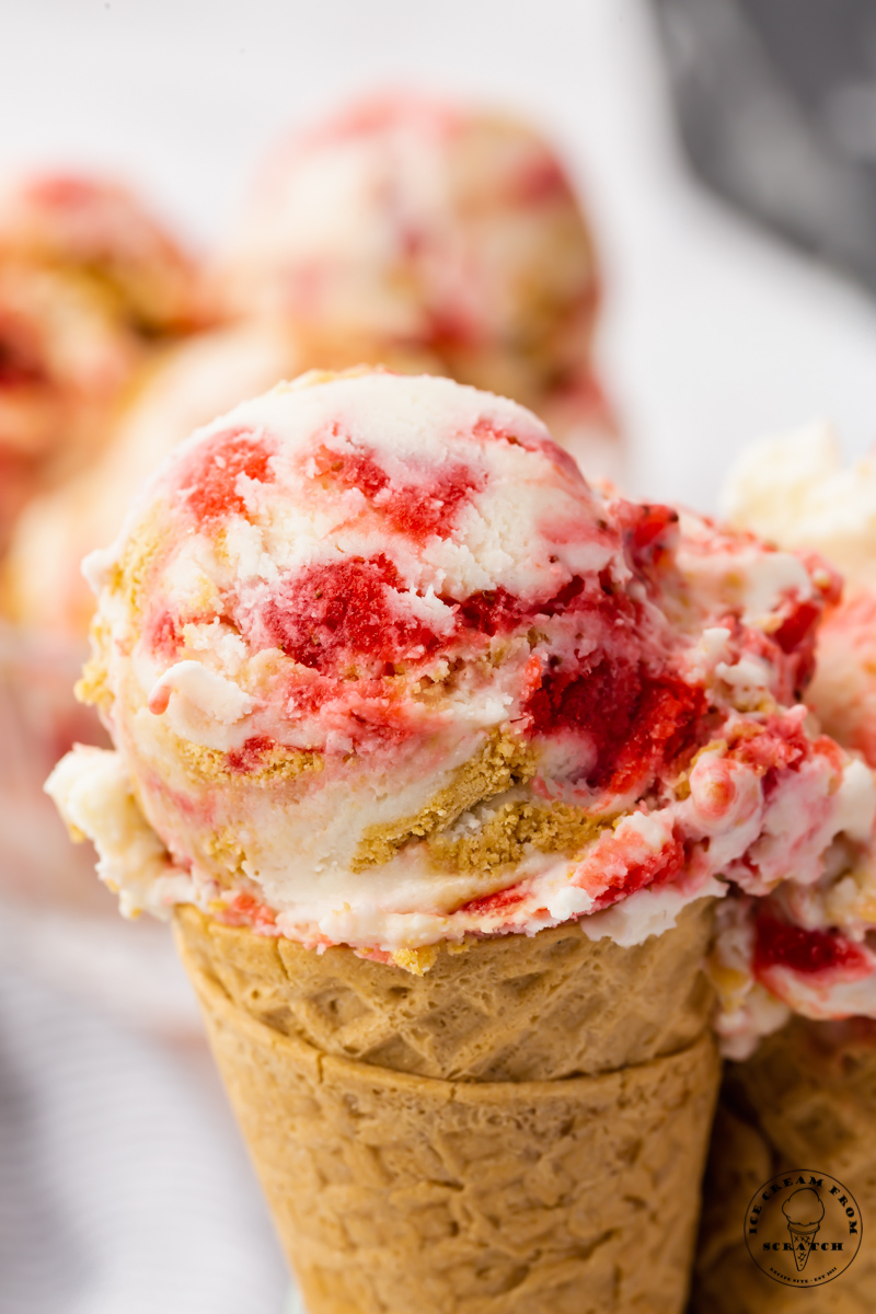 a sugar cone topped with cheesecake ice cream with big pieces of strawberries.