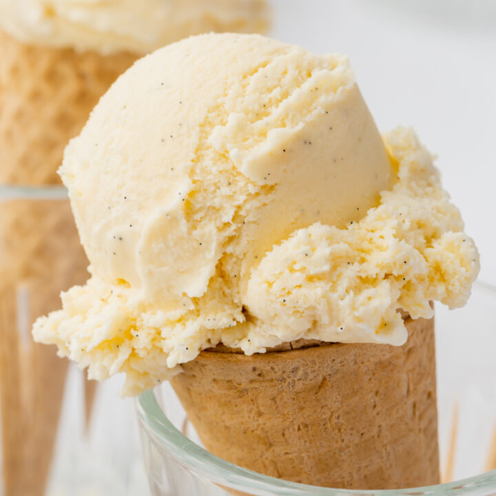 a sugar cone topped with a scoop of homemade vanilla bean ice cream, propped up in a glass.