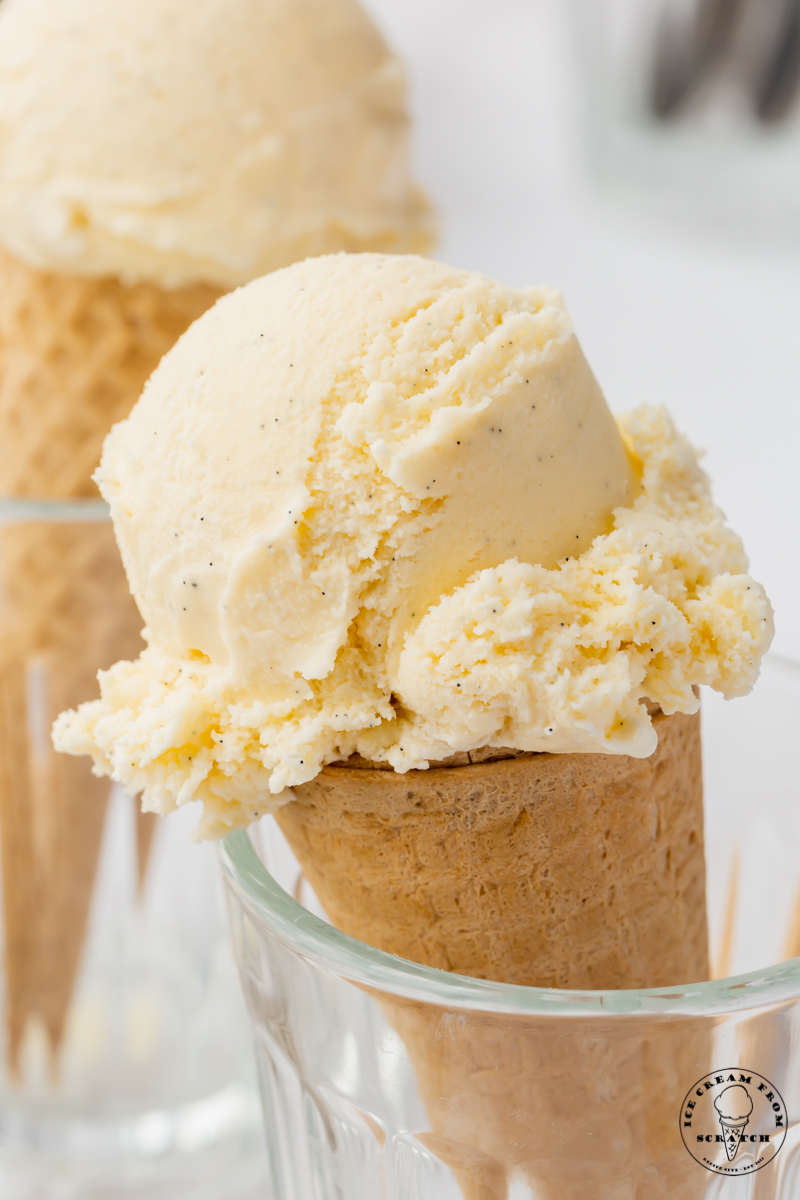 a sugar cone topped with a scoop of homemade vanilla bean ice cream, propped up in a glass.