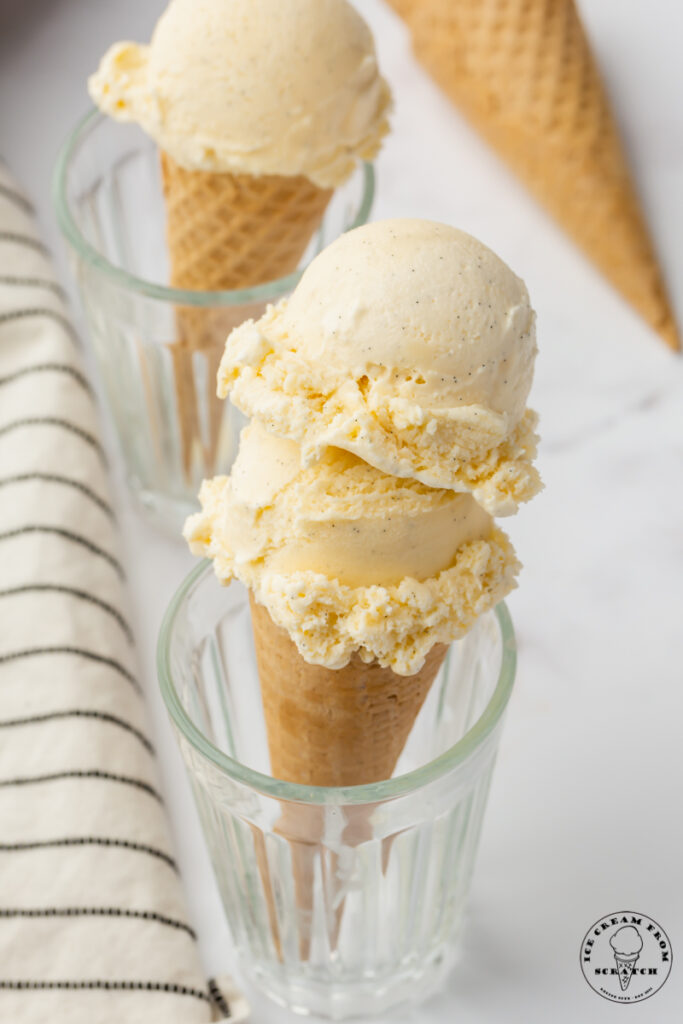 two glasses holding up sugar cones of vanilla bean ice cream.