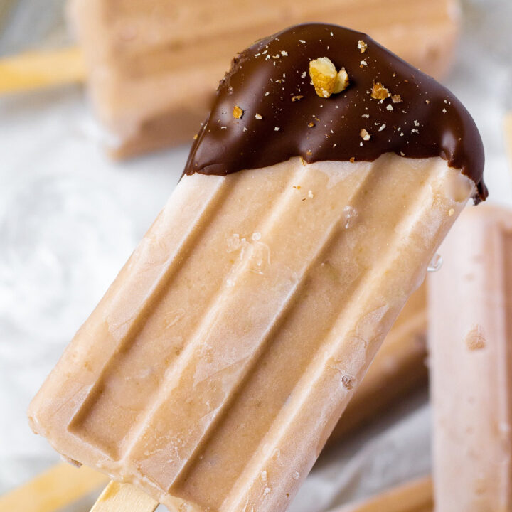 a light brown banana popsicle with just the top dipped in chocolate, sprinkled with chopped walnuts