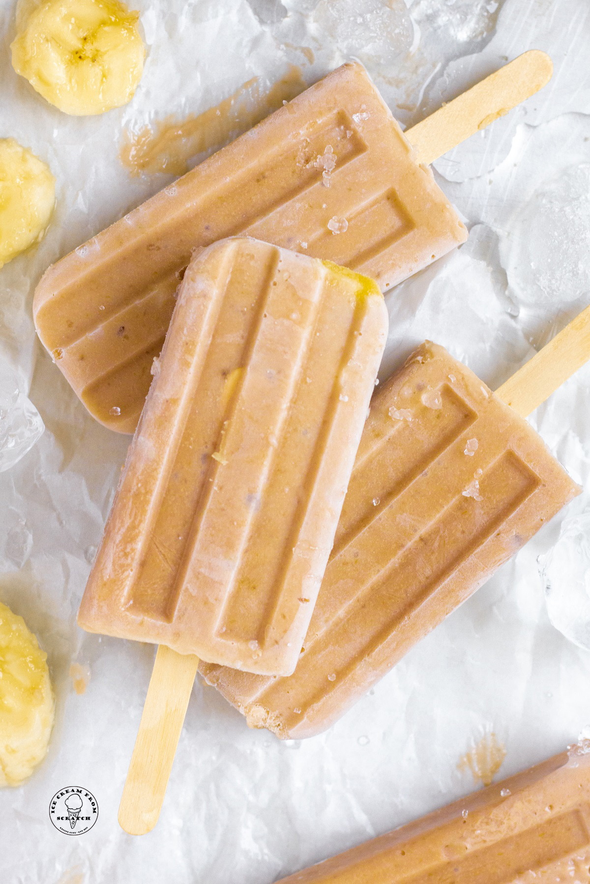 Three banana popsicles on a piece of parchment paper with slices of ripe banana