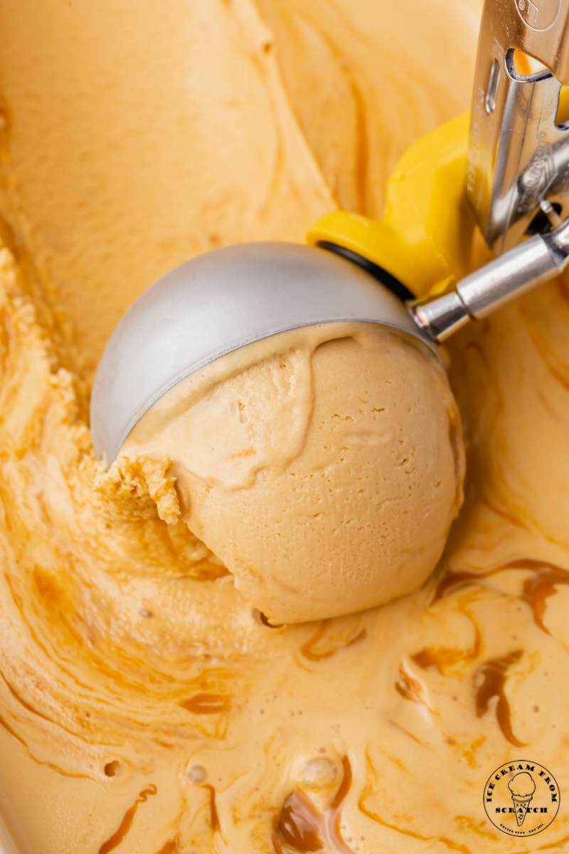Homemade dulce de leche ice cream with caramel swirl, being scooped with a metal ice cream scoop.