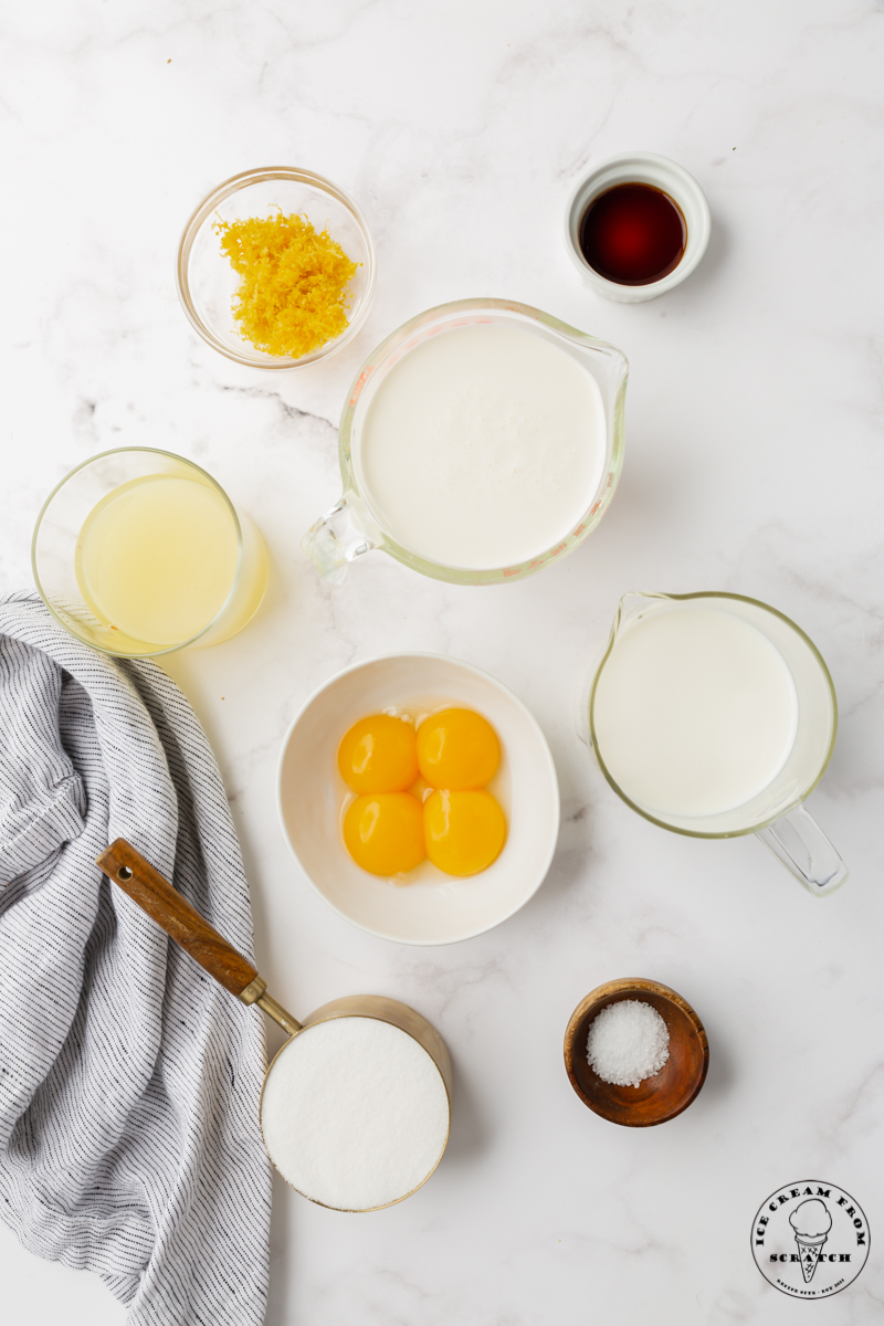 the 8 ingredients needed to make lemon ice cream from scratch, all measured into small bowls on a marble countertop.