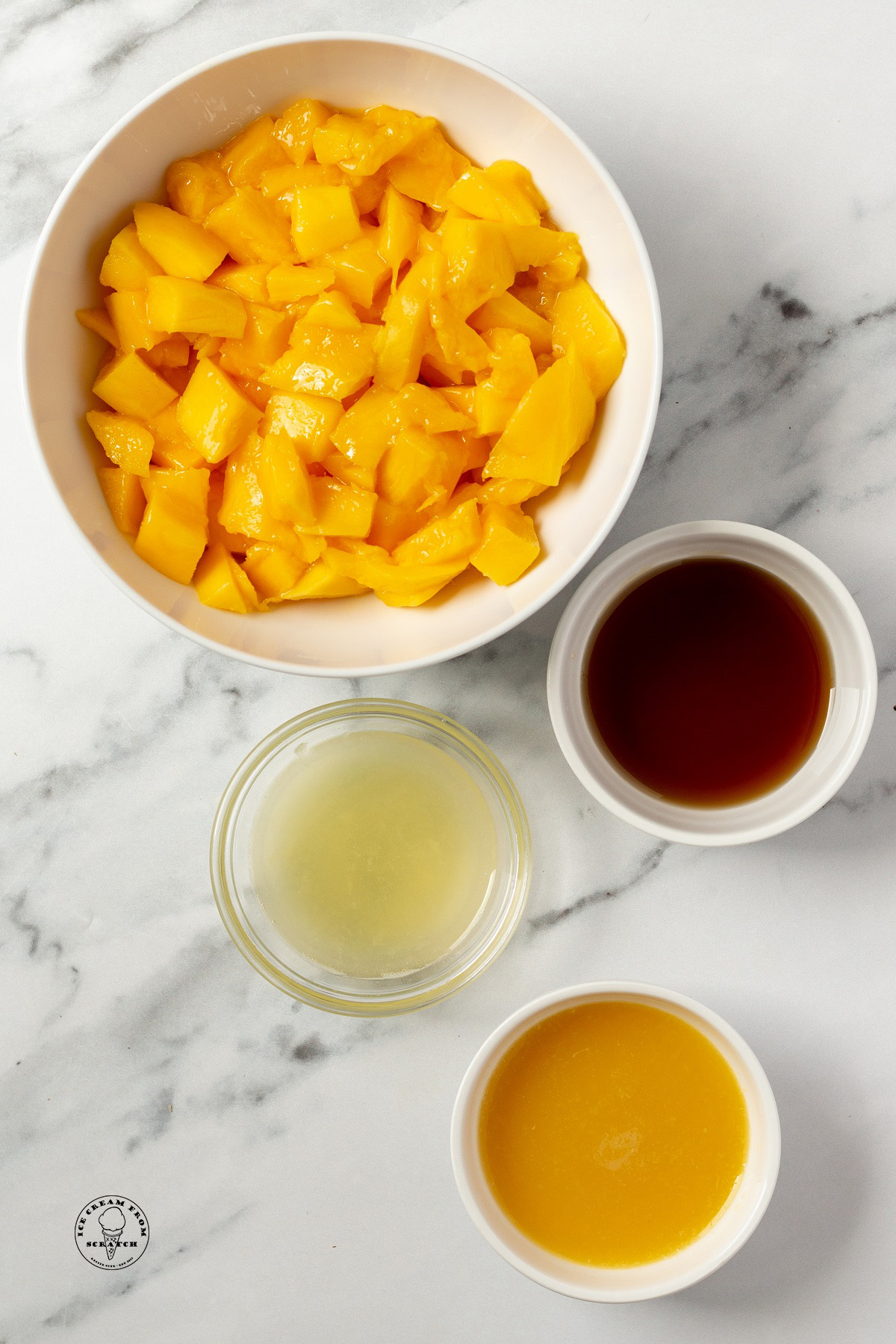 Four ingredients for making mango popsicles, measured into separate bowls, on a marble counter
