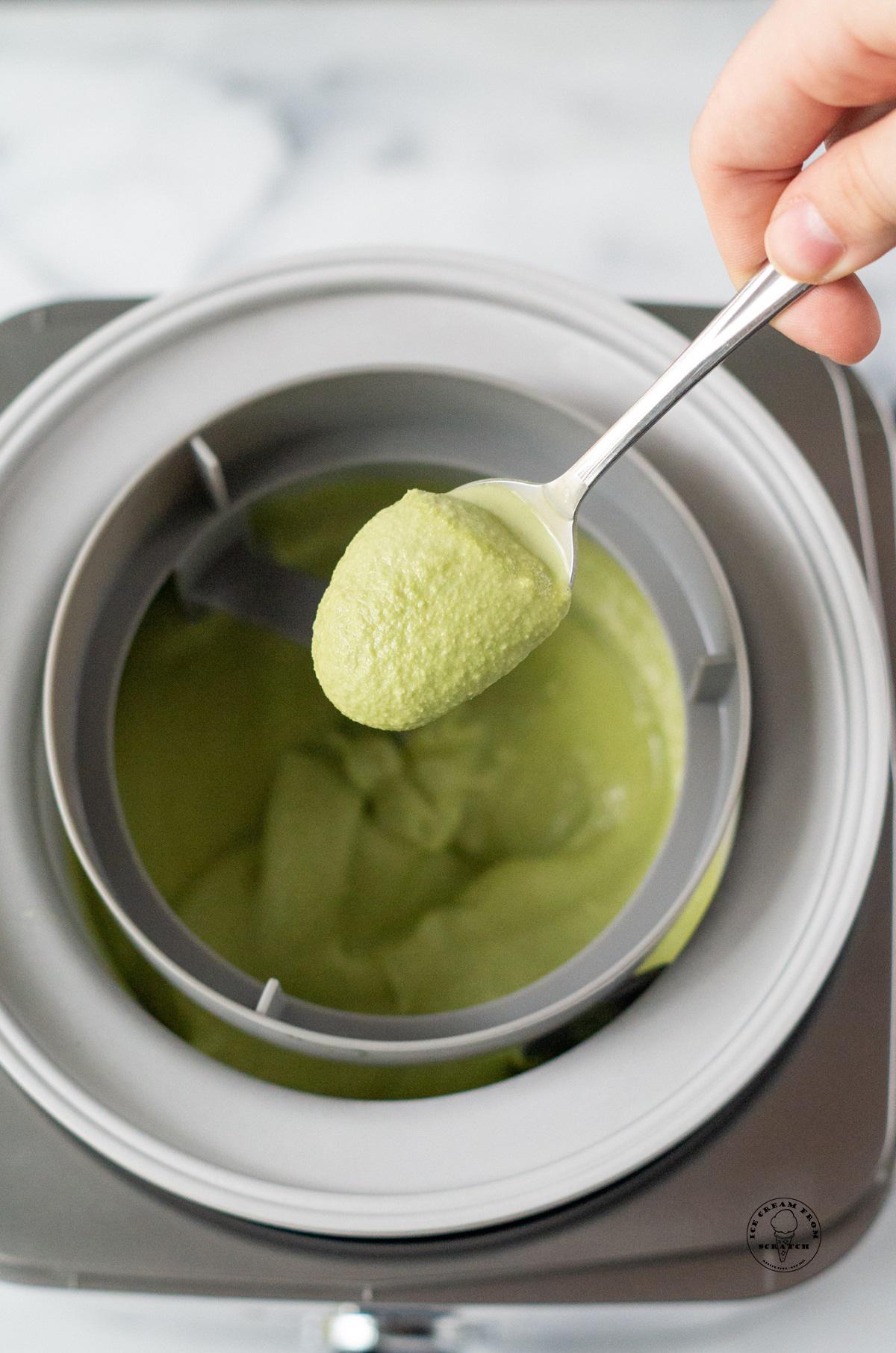 A spoon holding churned matcha ice cream up above the ice cream maker to show the soft texture.