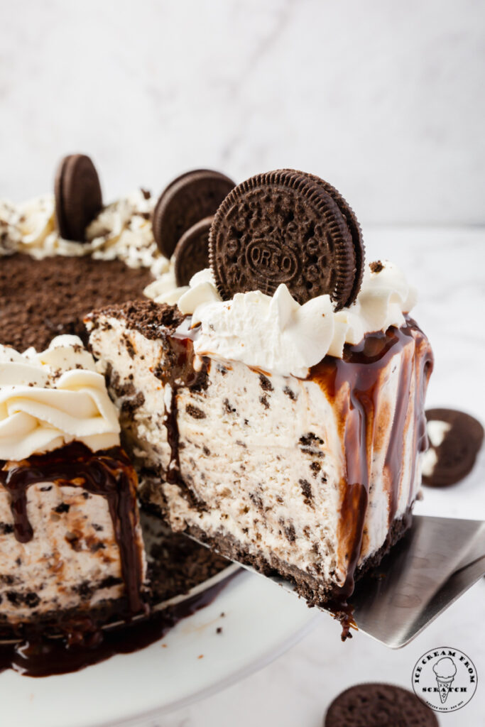 A slice of Oreo Ice cream cake, being lifted away from the full cake with a cake server.