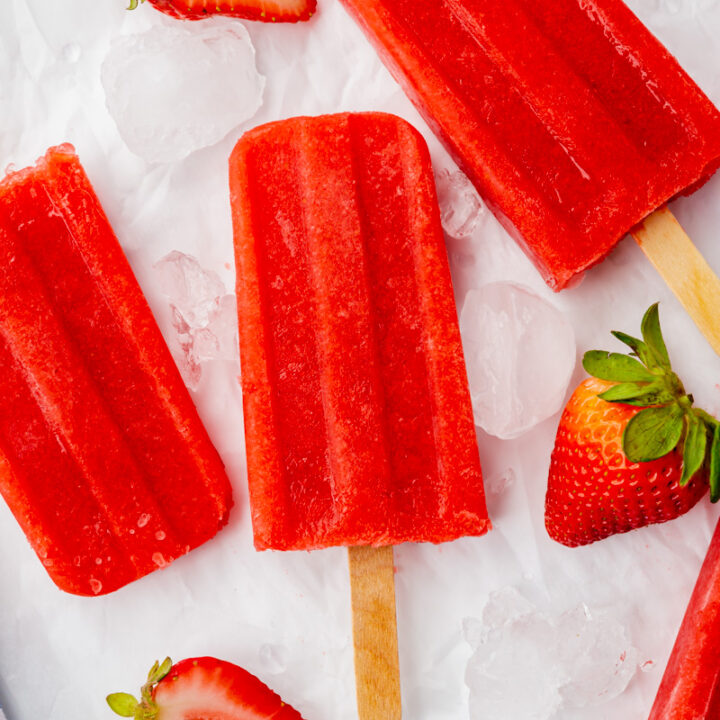 three strawberry popsicles on top of ice cubes with halved strawberries, viewed from above.