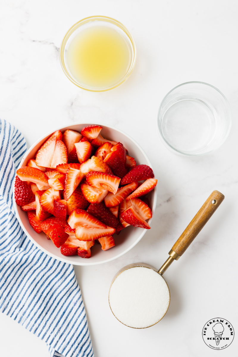 The ingredients needed to make strawberry popsicles, including berries, sugar, and lemon juice, measured into separate bowls, viewed from above.