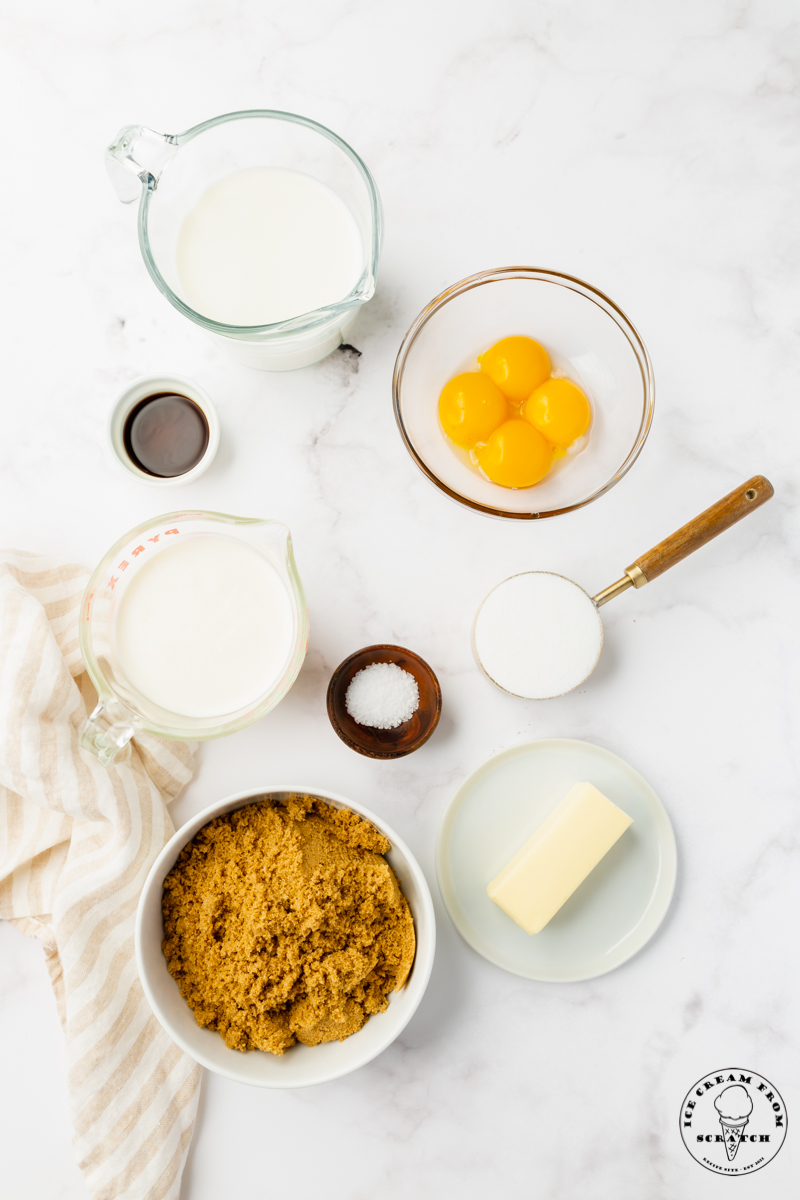 The ingredients for butterscotch ice cream: brown sugar, egg yolks, cream, butter, and more, in separate measuring bowls on a marble counter