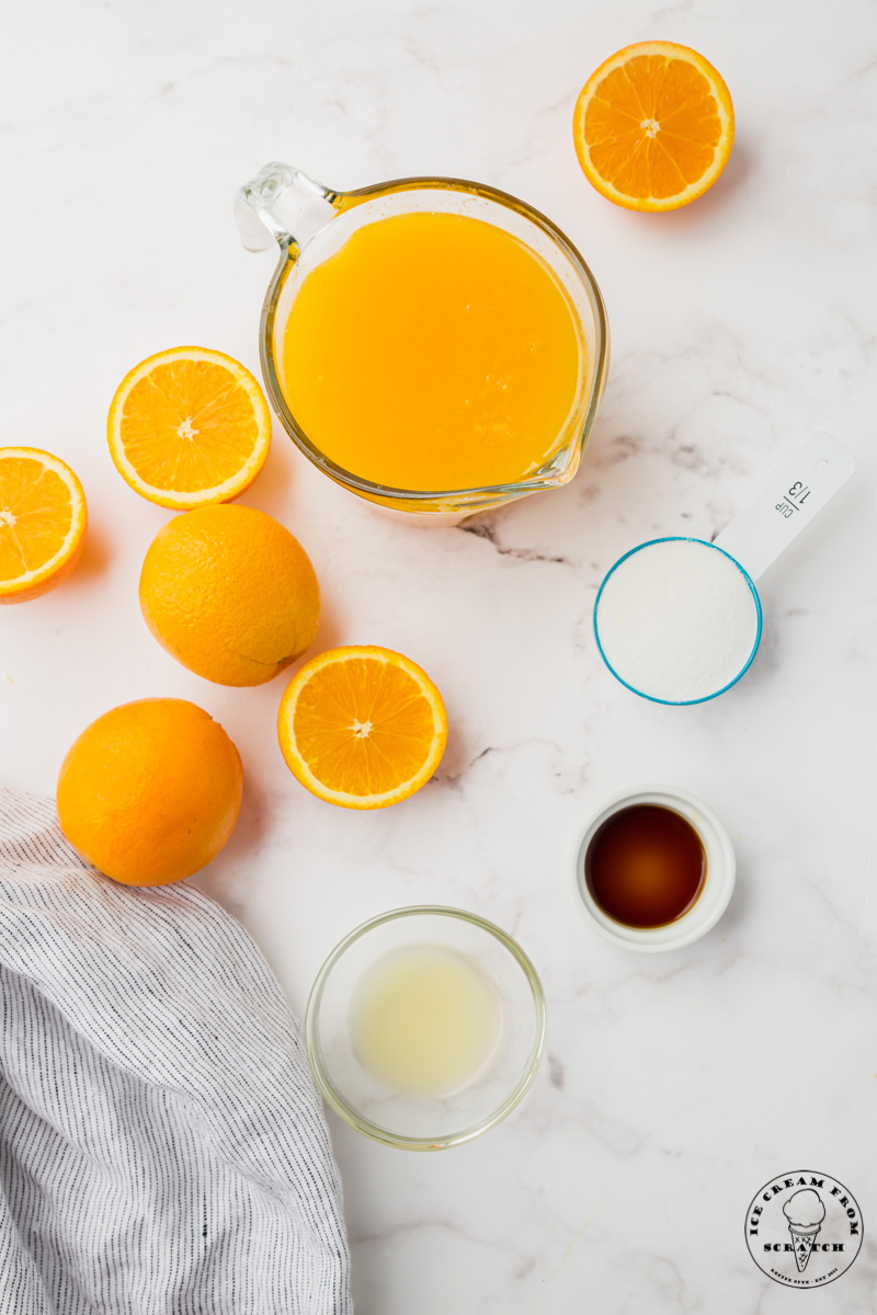 Fresh Orange Juice, and the other ingredients in orange popsicles, on a marble counter, viewed from above.