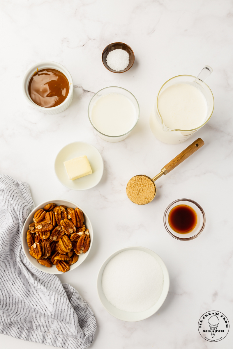 The ingredients for making pralines from scratch and homemade praline ice cream, all in separate bowls on a marble counter, viewed from above
