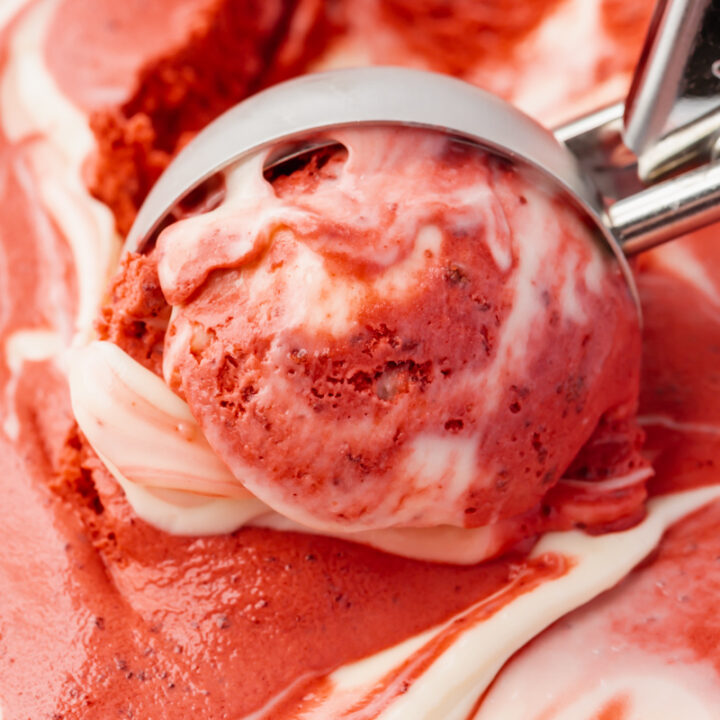 Red and white swirled red velvet ice cream, viewed from close up as it's scooped with an ice cream scoop