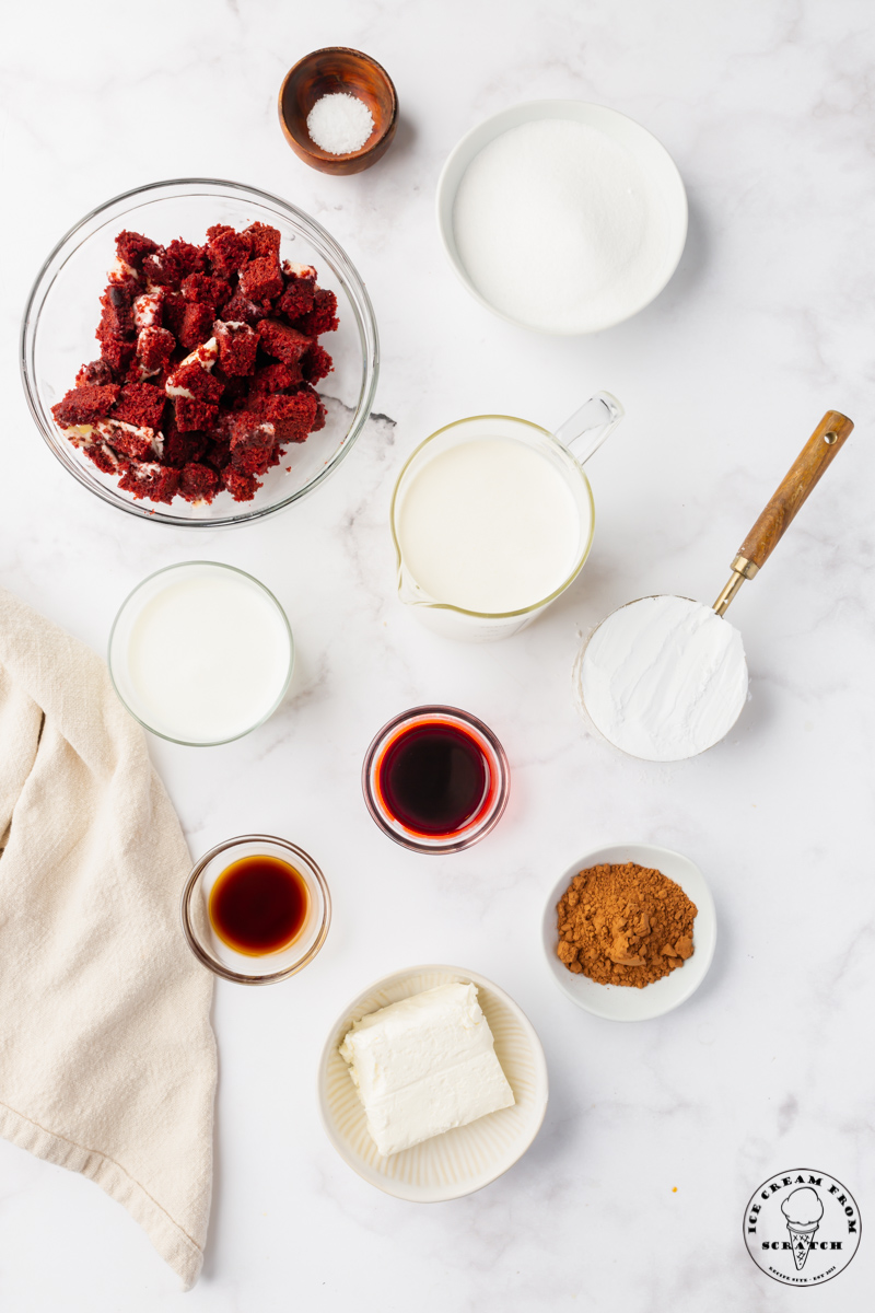The ingredients for making homemade red velvet ice cream, all in separate bowls in a marble counter, including pieces of cake and cream cheese.