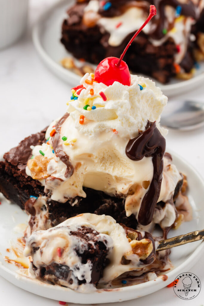 a brownie sundae on a plate. A spoon has removed a bite from the sundae and is now on the edge of the plate.
