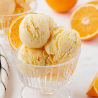 a ridged glass ice cream dish filled with scoops of homemade orange ice cream, garnished with an orange slice.