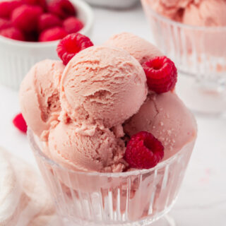 a glass footed dish filled with 5 scoops of homemade raspberry ice cream, garnished with fresh berries.