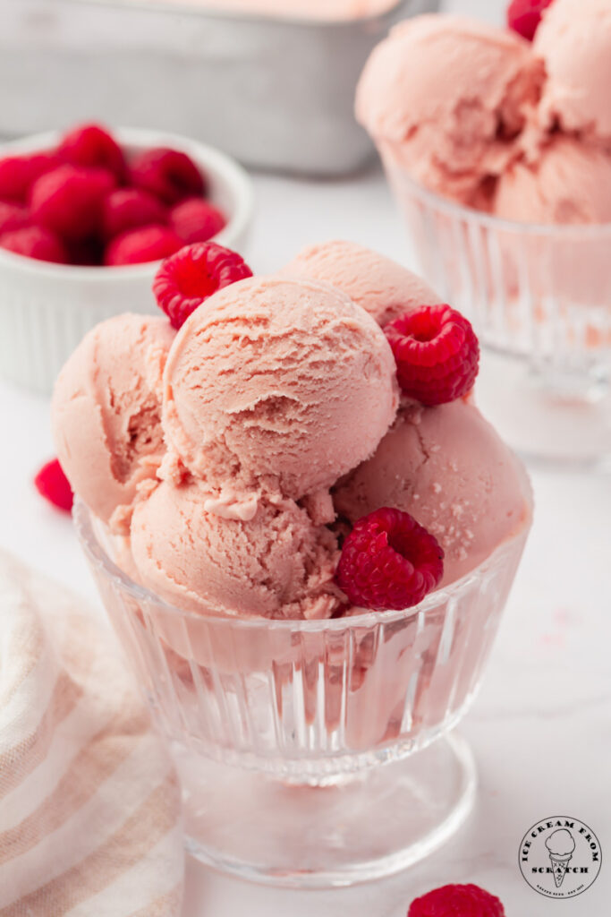 a glass footed dish filled with 5 scoops of homemade raspberry ice cream, garnished with fresh berries.