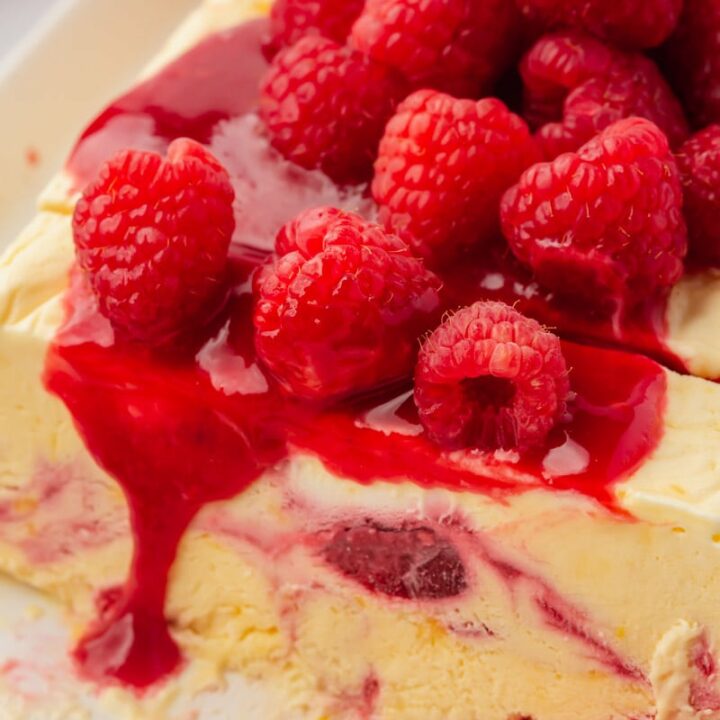 Closeup view of a raspberry semifredo that has been sliced. It's topped with homemade raspberry sauce and fresh berries