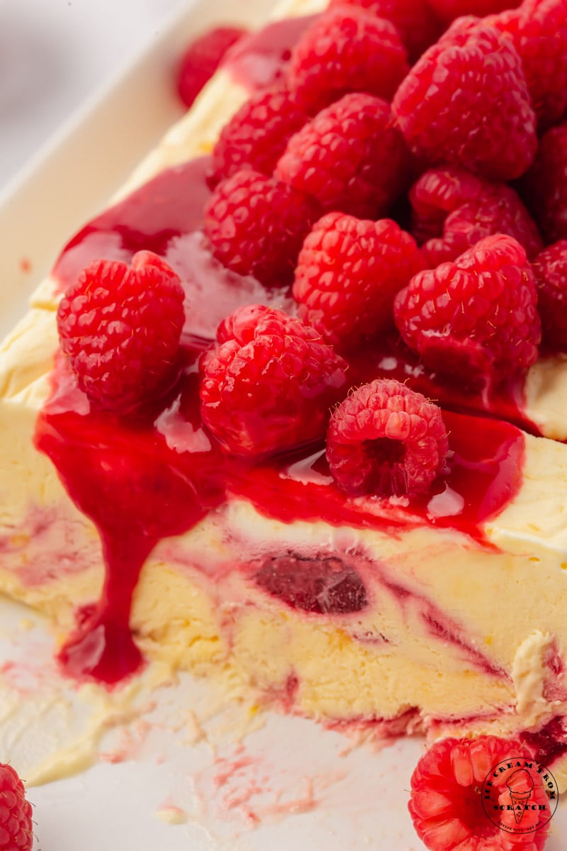 Closeup view of a raspberry semifredo that has been sliced. It's topped with homemade raspberry sauce and fresh berries