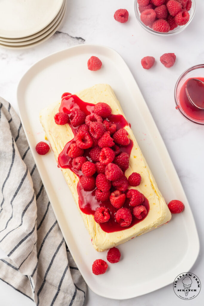a rounded rectangular platter holding a rectangle shaped semifreddo topped with raspberry sauce and fresh raspberries. Viewed from overhead.