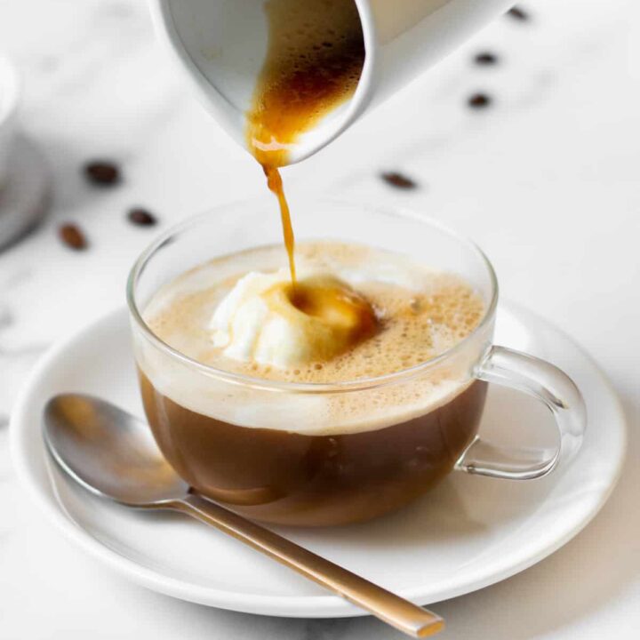 a small pitcher pouring espresso into an affogato in a clear mug.