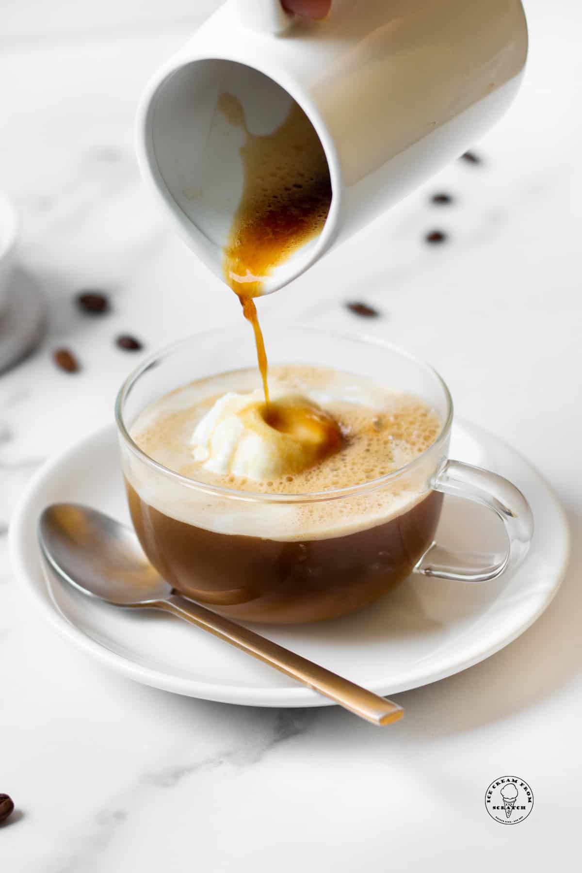 a small pitcher pouring espresso into an affogato in a clear mug.