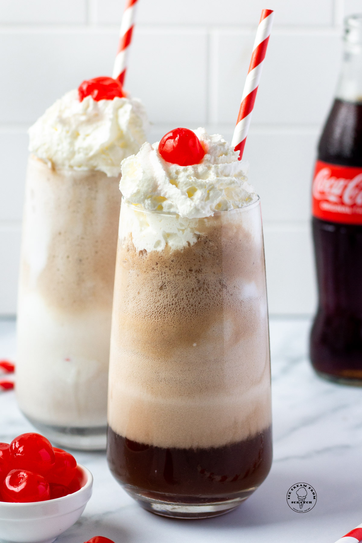Two tall coke floats topped with whipped cream and a cherry.
