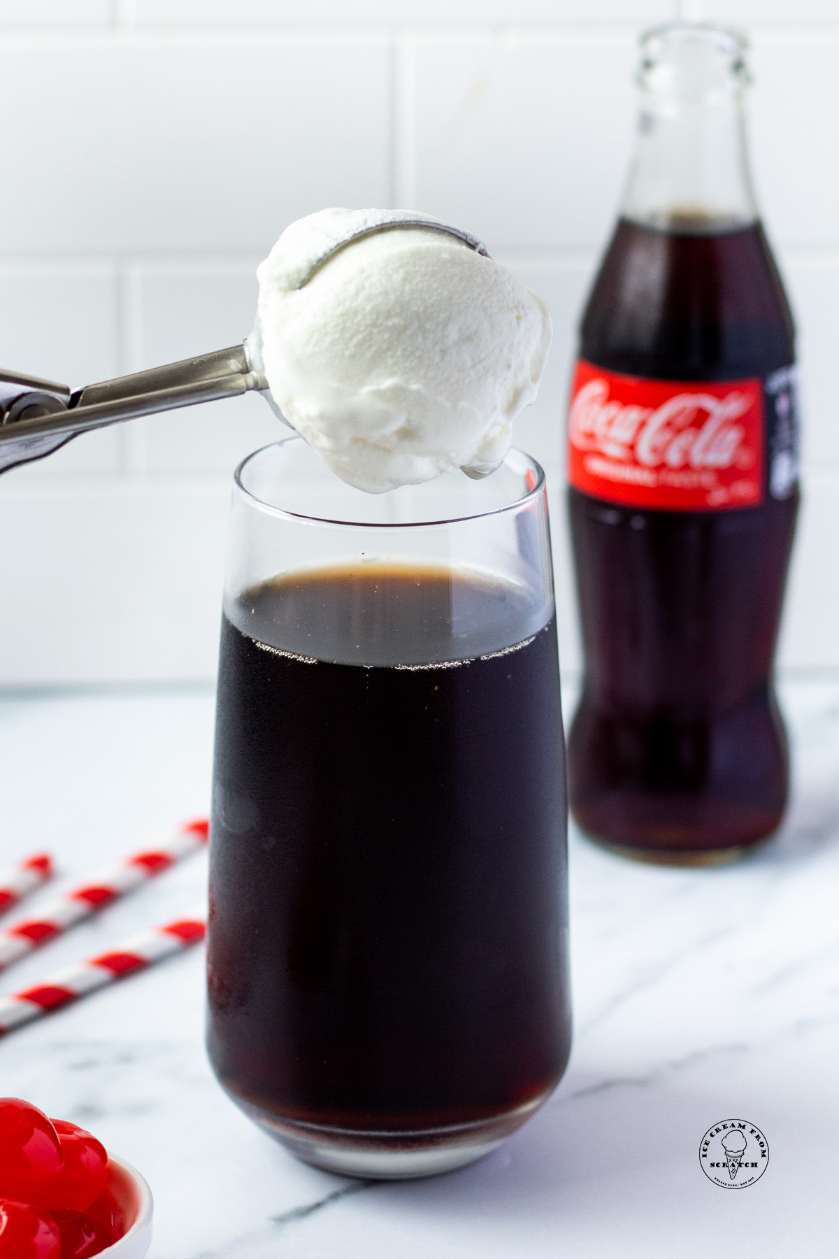 a glass of coke with a scoop of vanilla ice cream being added.