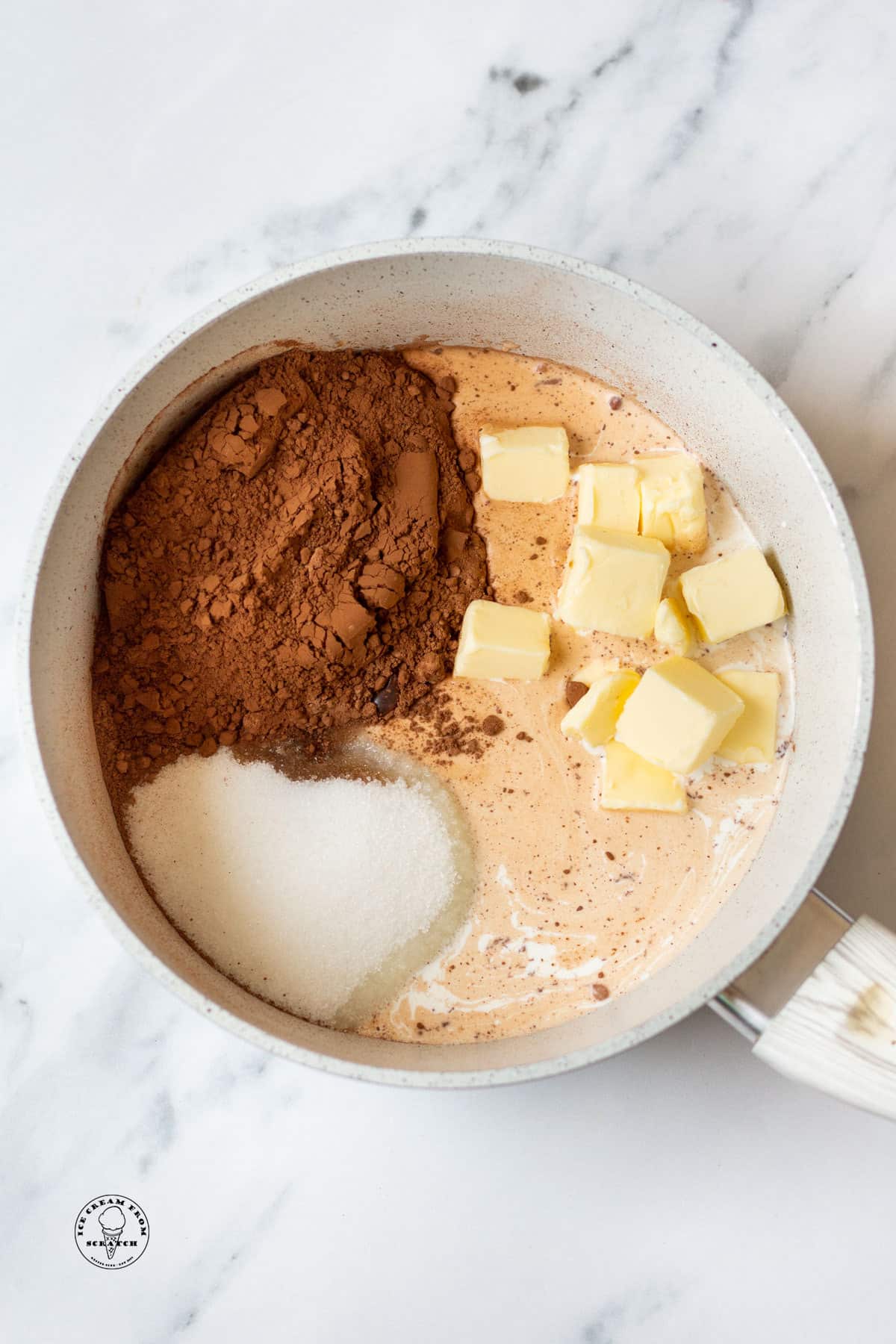 the ingredients for hot fudge sauce, in a saucepan, including sugar, cocoa powder, and cubed butter.