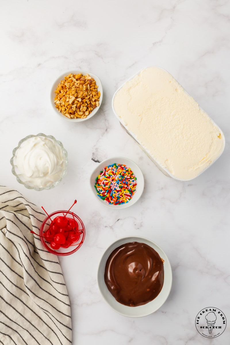 The ingredients needed to make a classic hot fudge sundae, all on a counter, viewed from above.