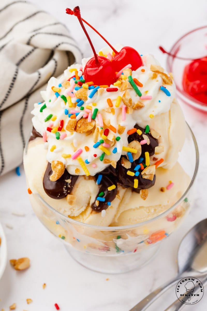 a sundae topped with hot fudge, whipped cre3am, rainbow sprinkles, peanuts, and two cherries