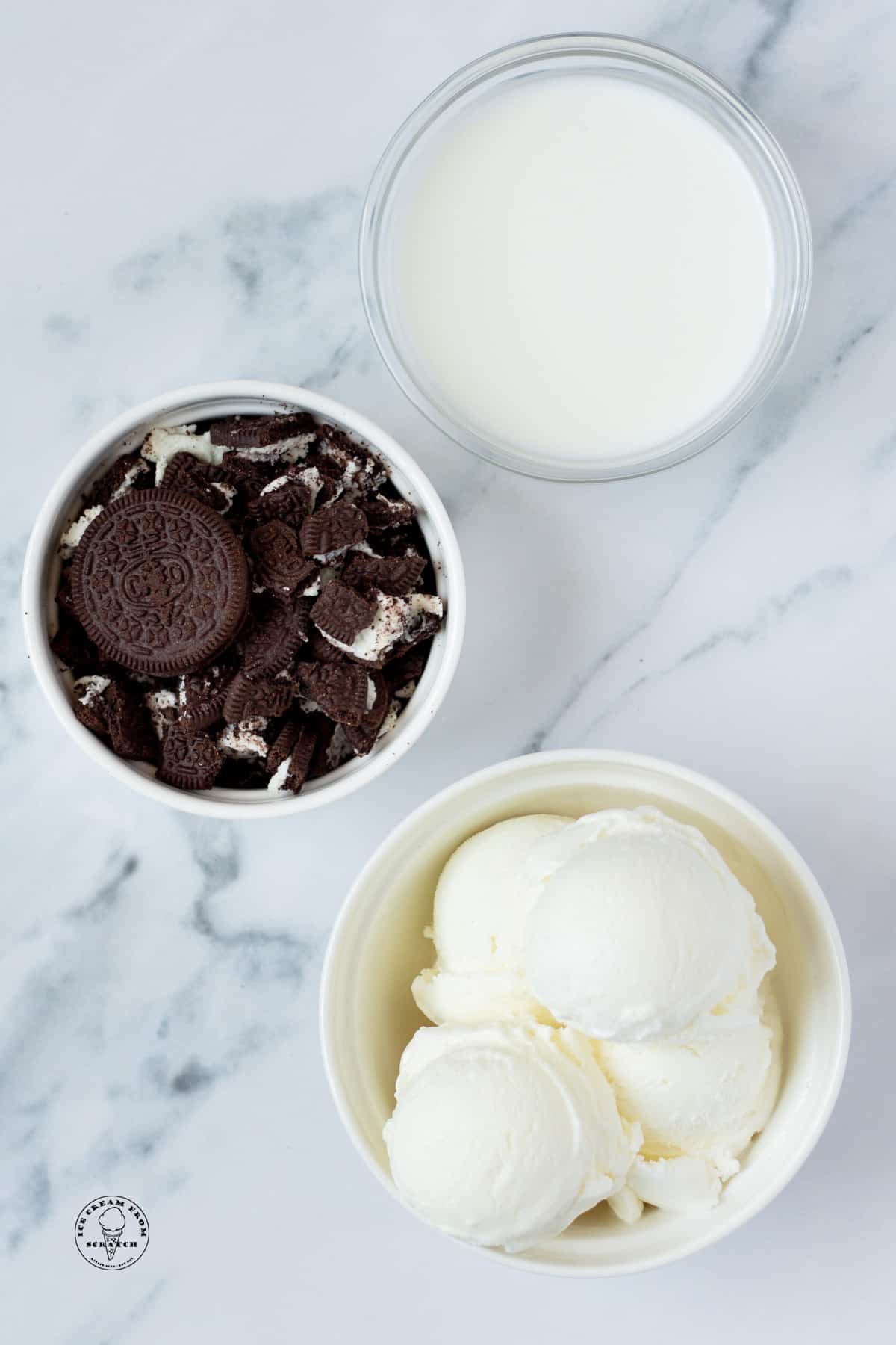 a bowl of crushed oreos, a bowl of milk, and a bowl of vanilla ice cream, on a marble counter, viewed from above.,