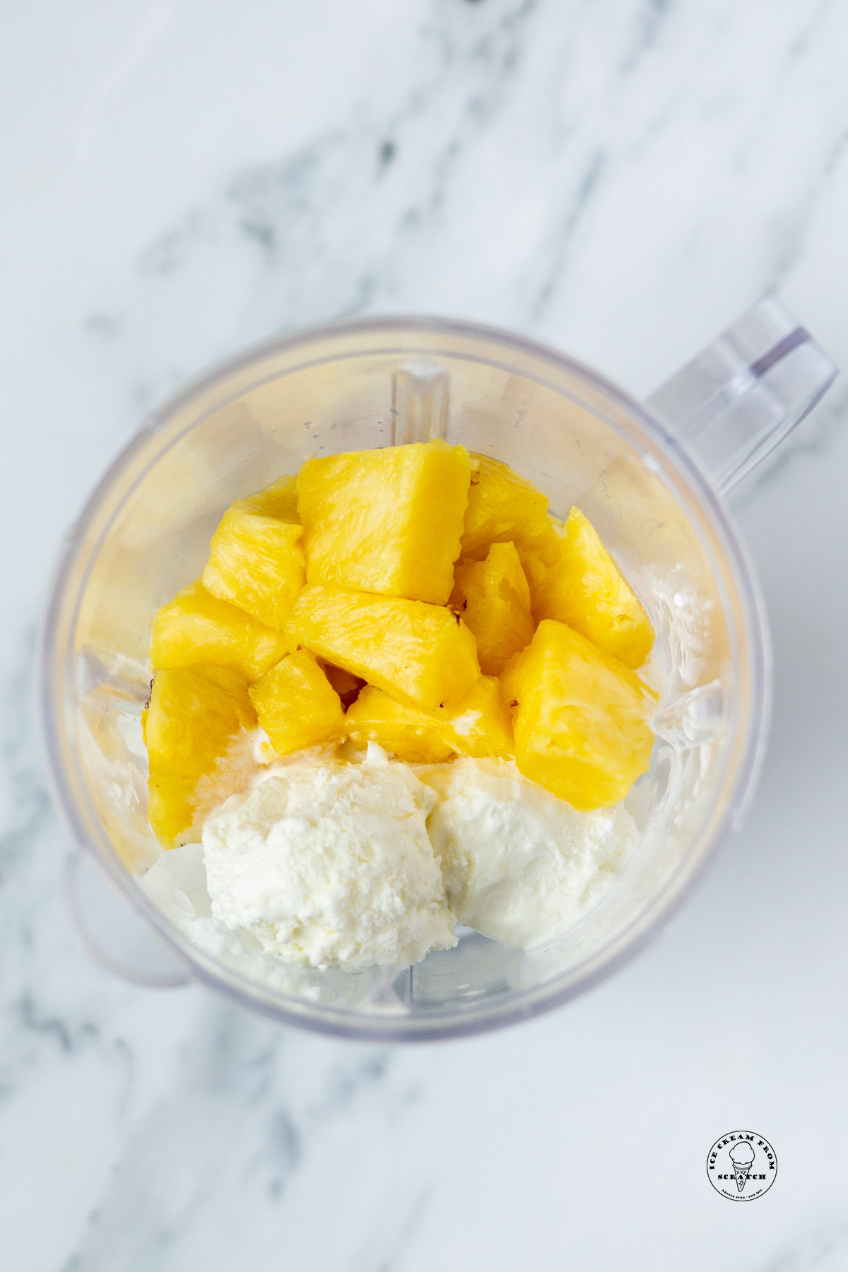 Pineapple pieces and vanilla ice cream in a blender, viewed from overhead