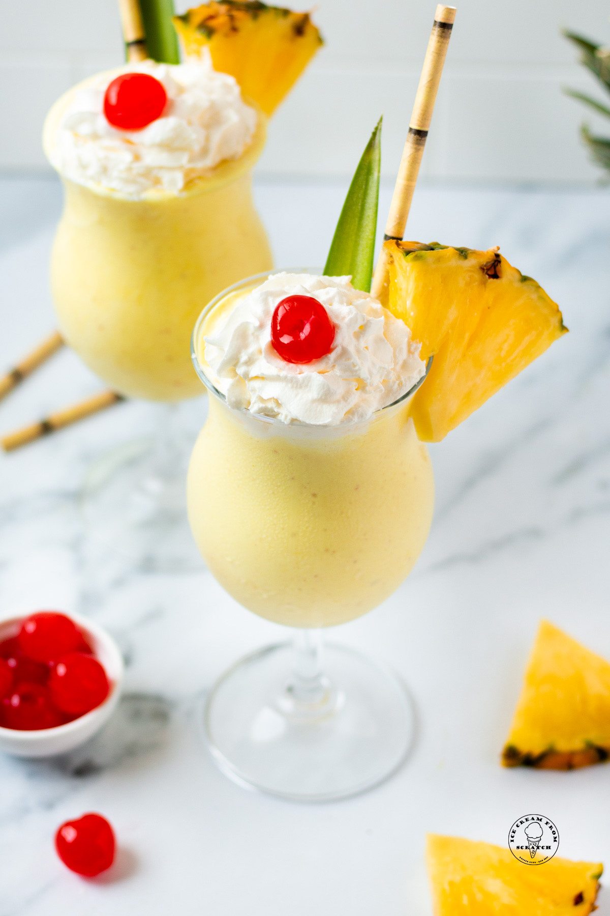 Looking down on two pineapple milkshakes garnished with cherries, pineapple slices, and bamboo straws