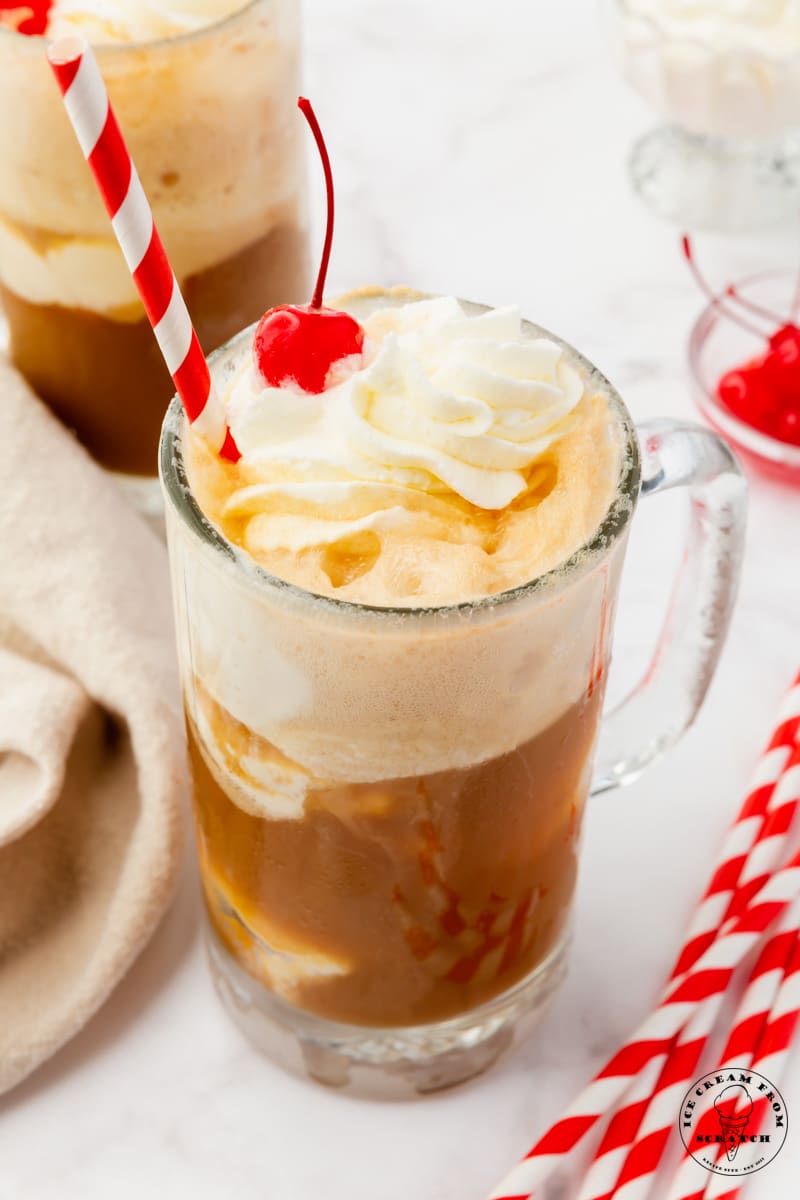 a root beer float in a clear frosted mug, with a red and white striped straw.