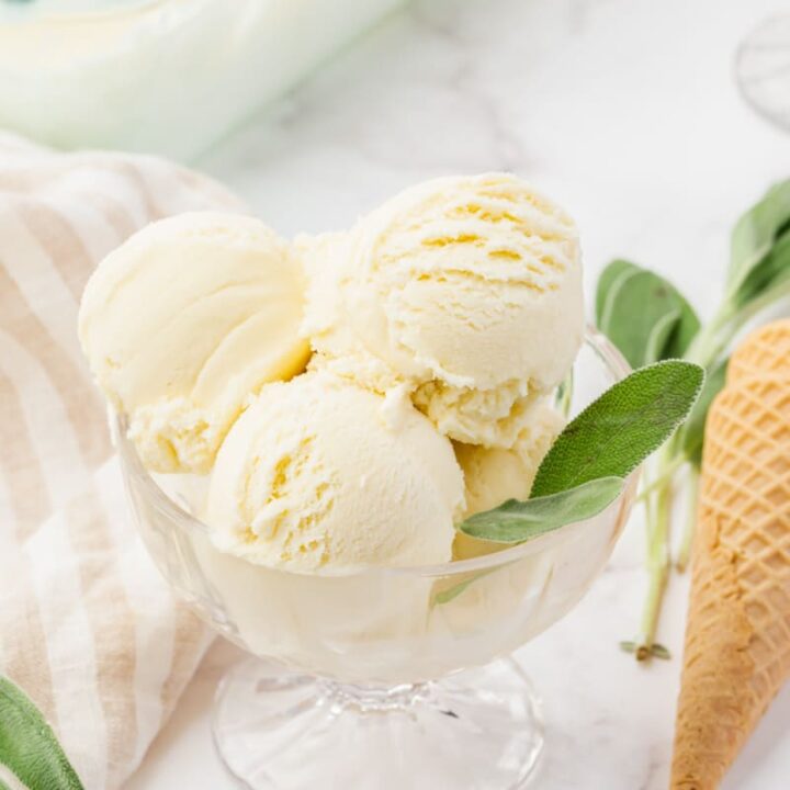 a footed glass bowl of sage ice cream, garnished with fresh sage leaves.
