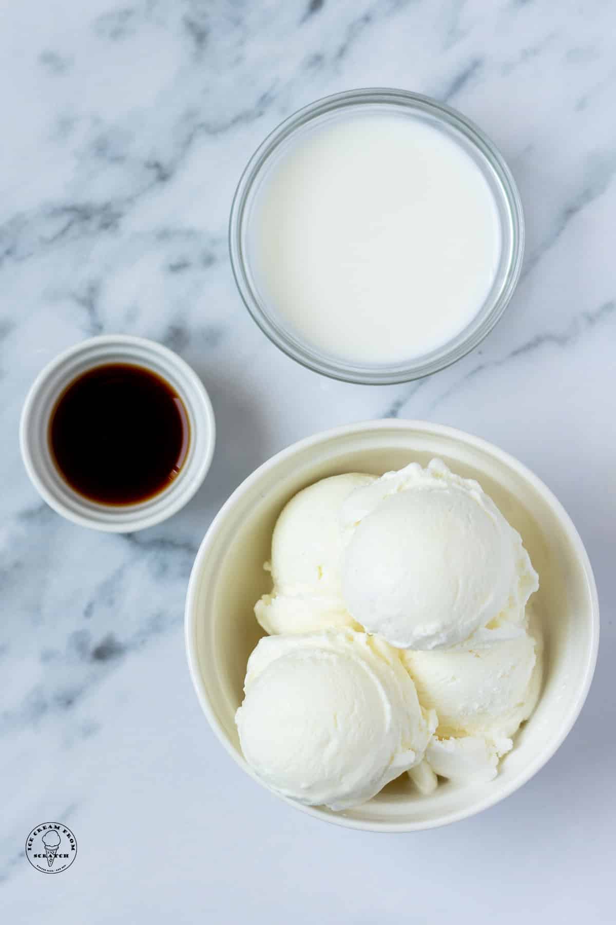 a bowl of vanilla ice cream, a bowl of milk, and a bowl of vanilla extract on a marble counter, viewed from above