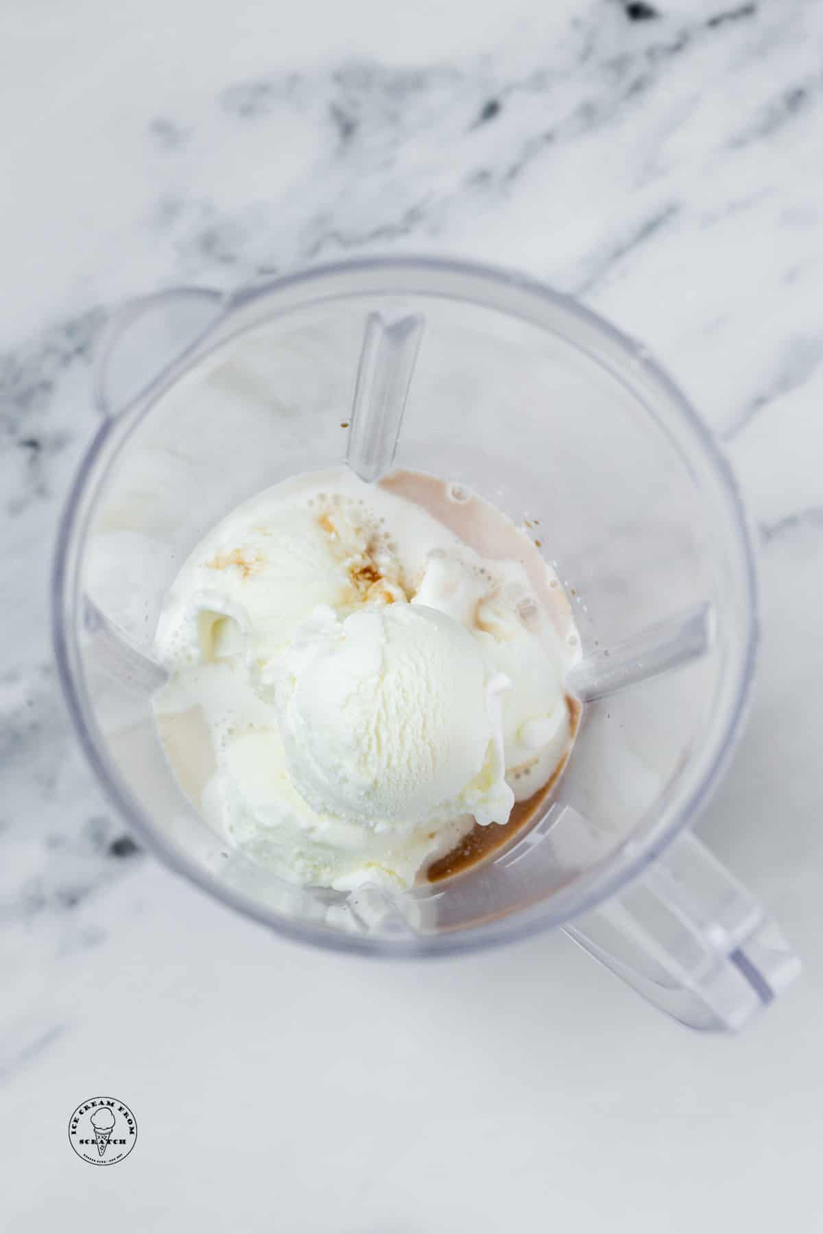 The ingredients for a vanilla milkshake in a blender jar, viewed from above