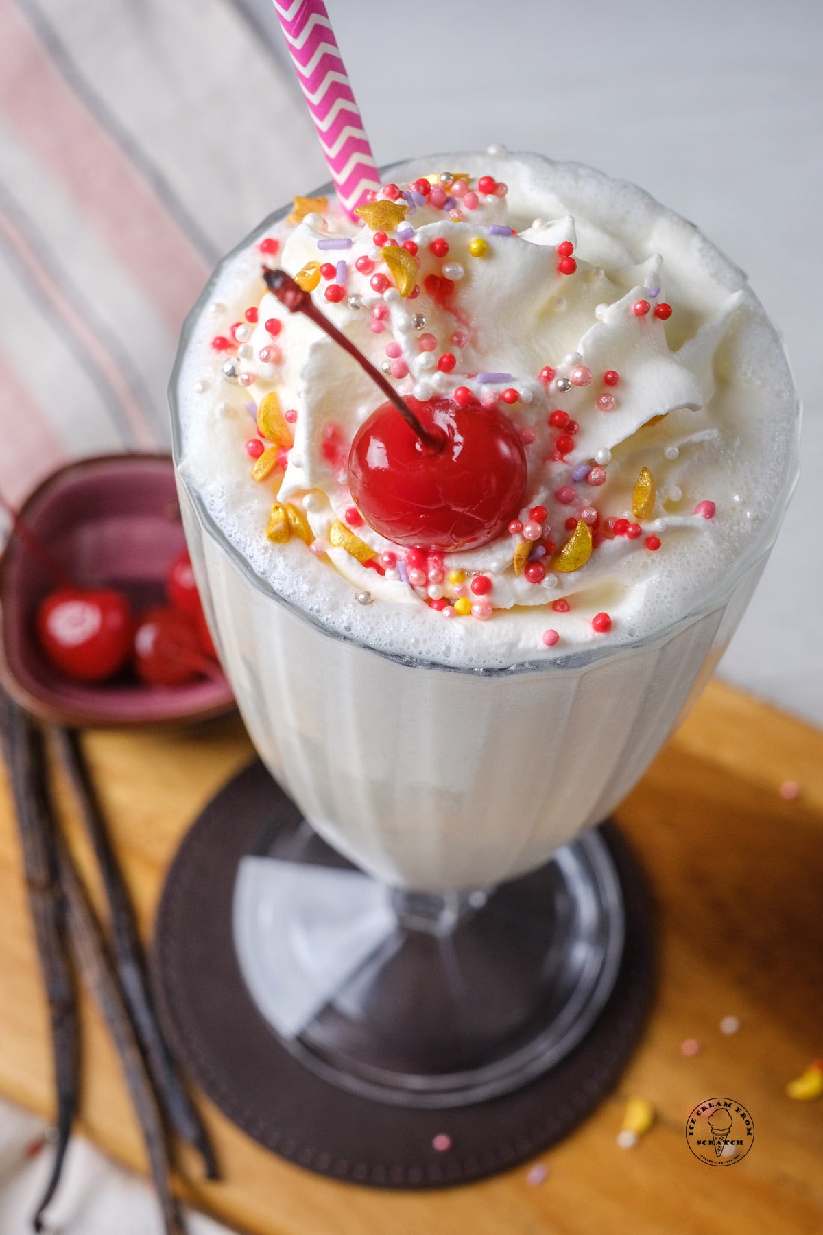 a vanilla milkshake with whipped cream, a cherry, and colorful pink and gold sprinkles.