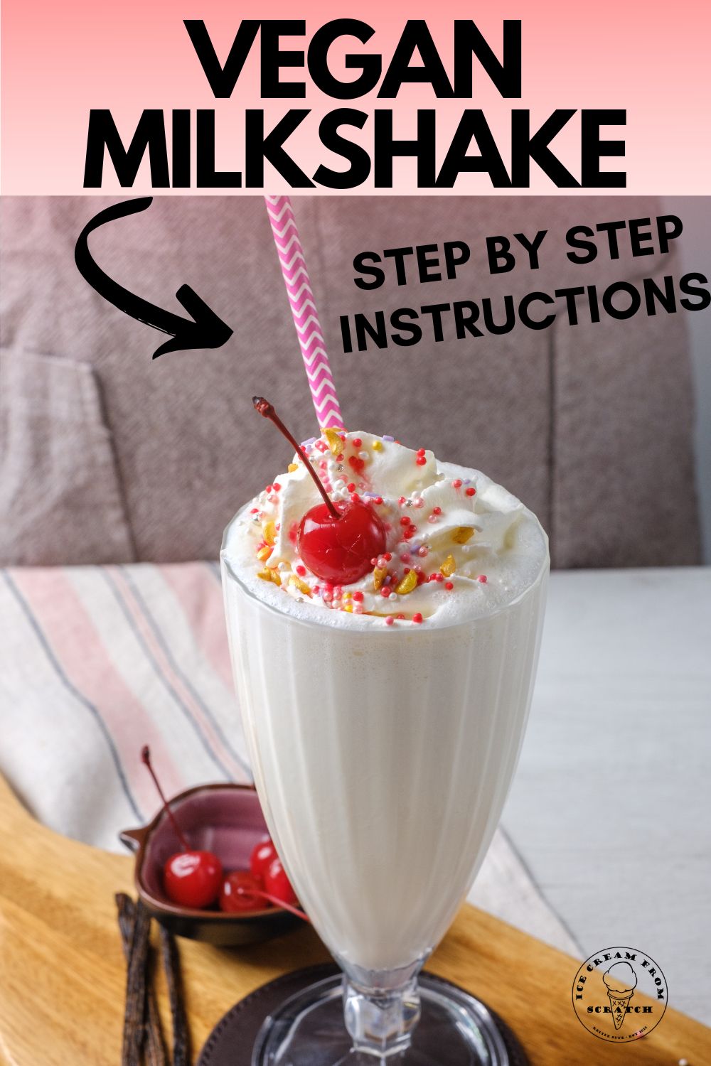 a footed milkshake glass on a leather coaster on a wooden cutten board. The glass is filled with a vegan vanilla milkshake topped with sprinkles, whipped cream, and a cherry. text at top of image says "vegan milkshake, step by step instructions"