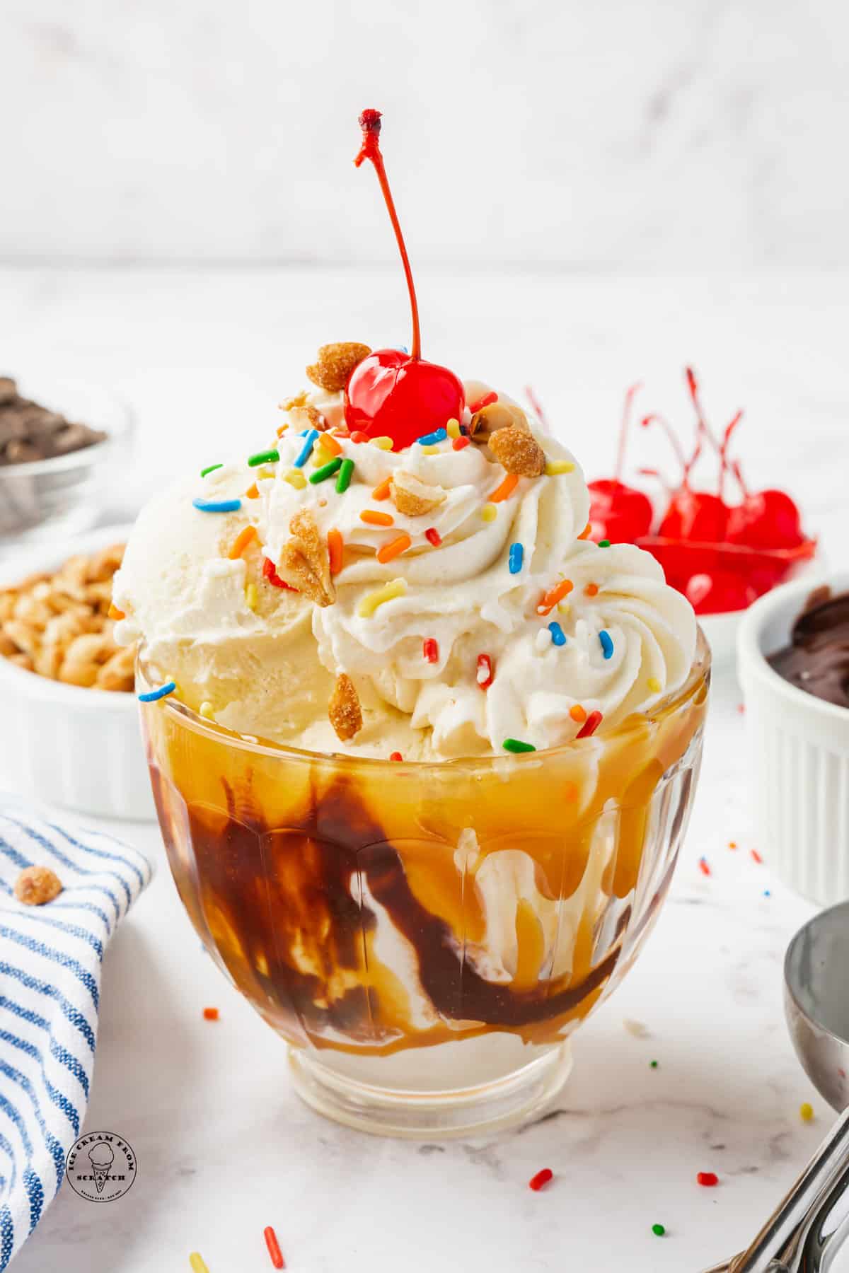 a glass sundae dish filled with a caramel sundae topped with whipped cream, sprinkles, and a cherry.