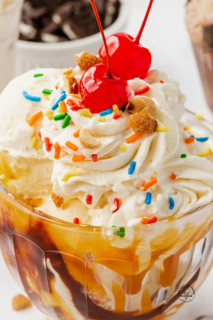 Closeup photo of a caramel sundae topped with nuts, cherries, sprinkles.