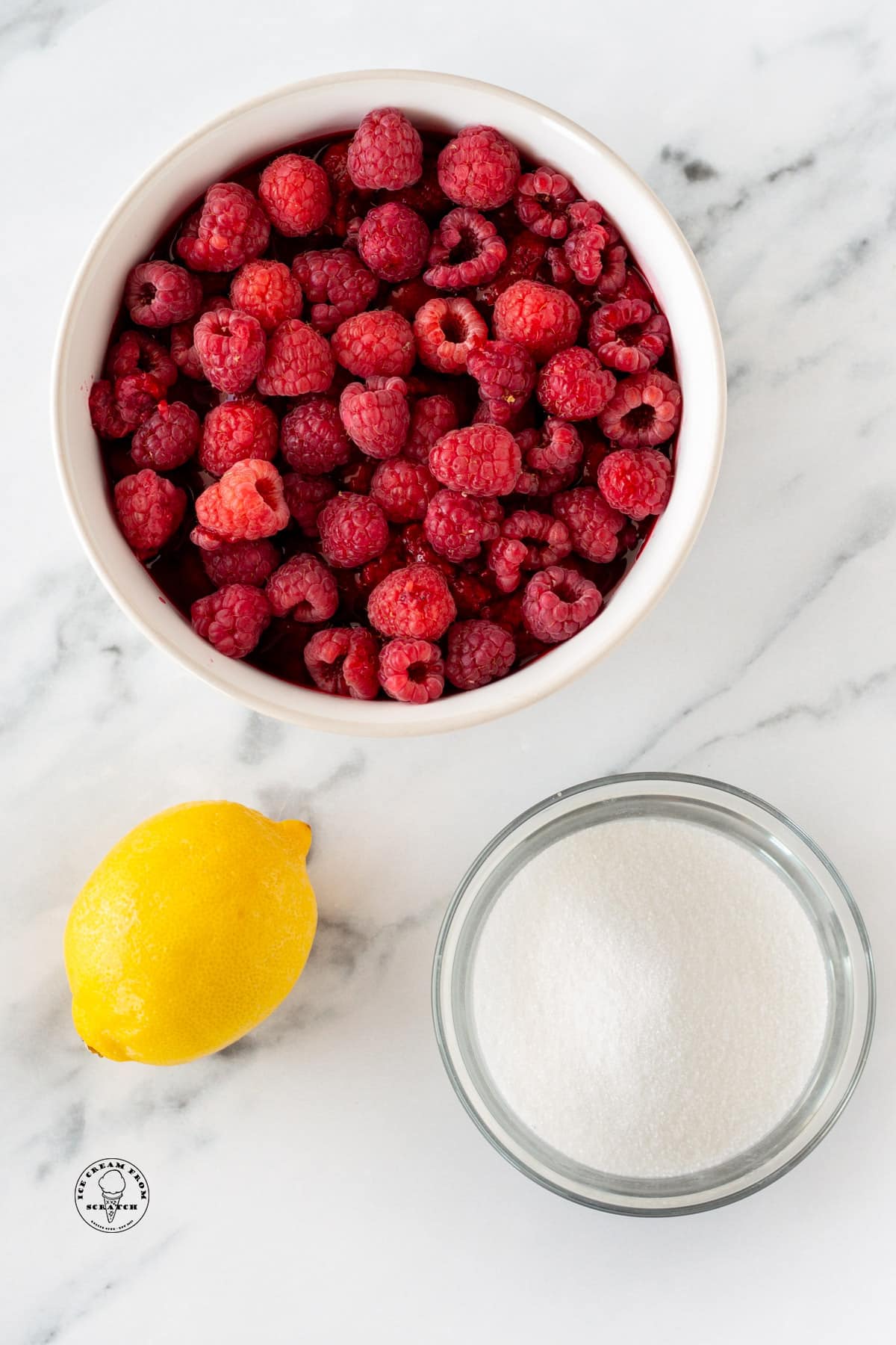 A bowl of raspberries, a bowl of sugar, and a lemon.