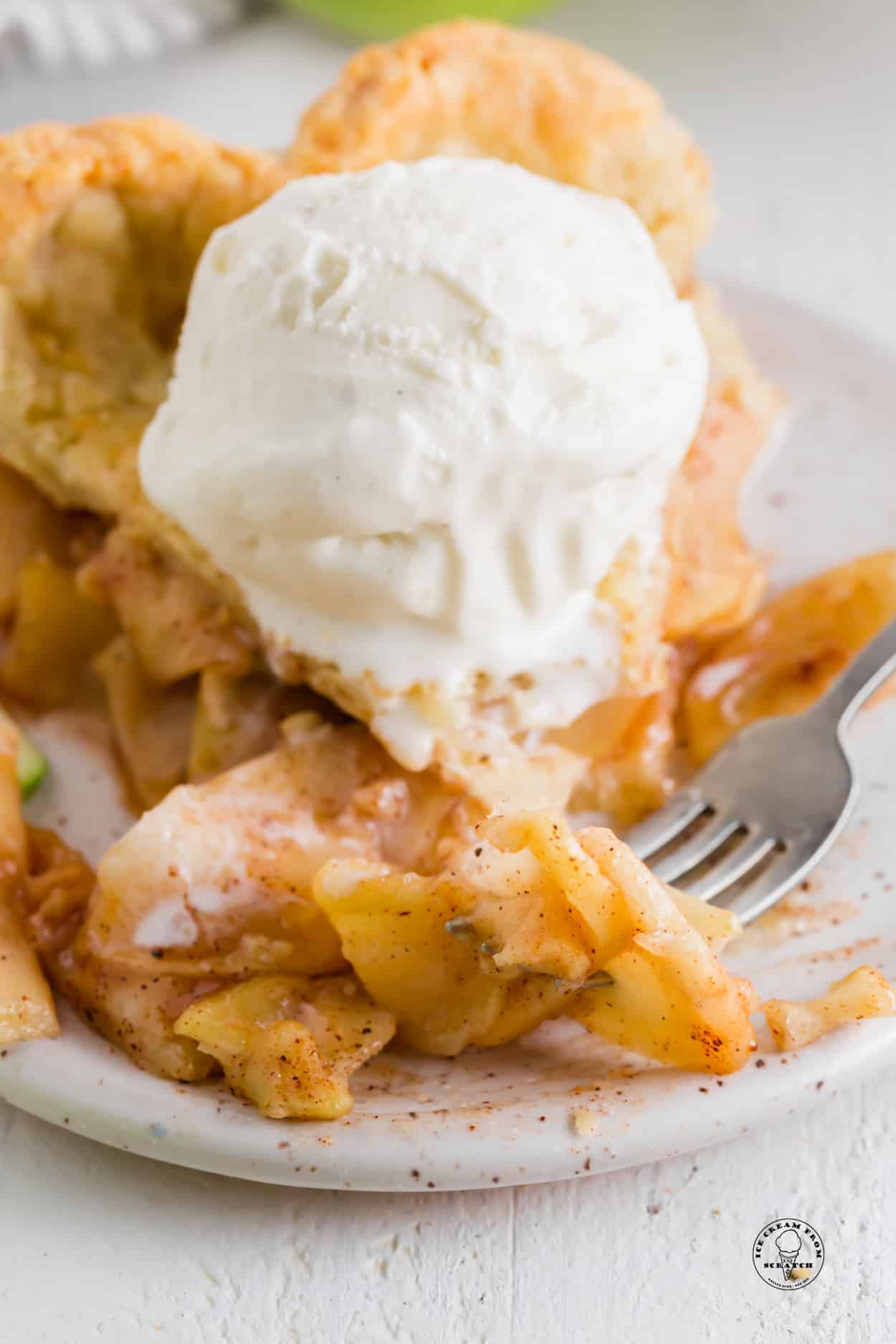 a slice of apple pie with cinnamon, topped with a scoop of vanilla ice cream.