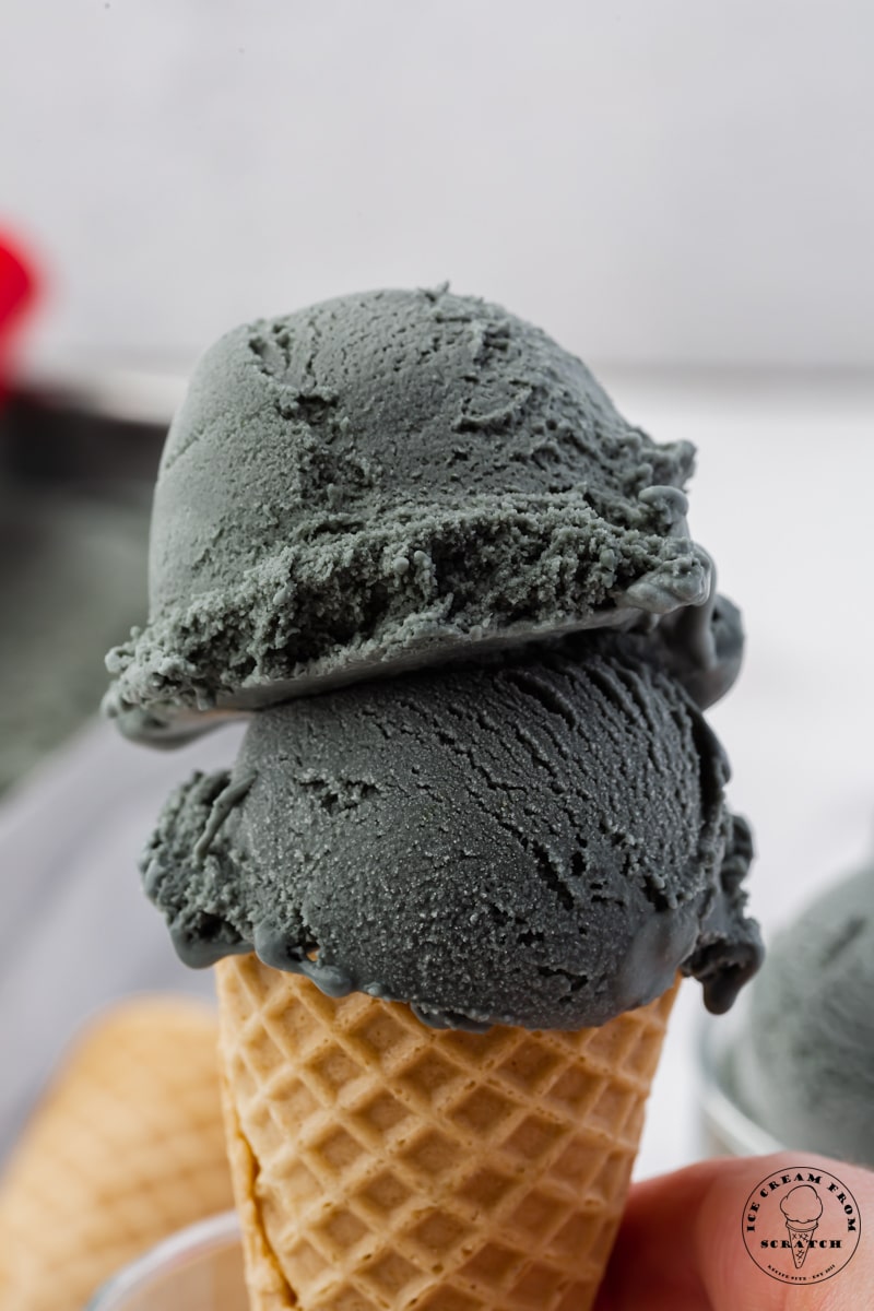 Two scoops of black licorice ice cream on a sugar cone.