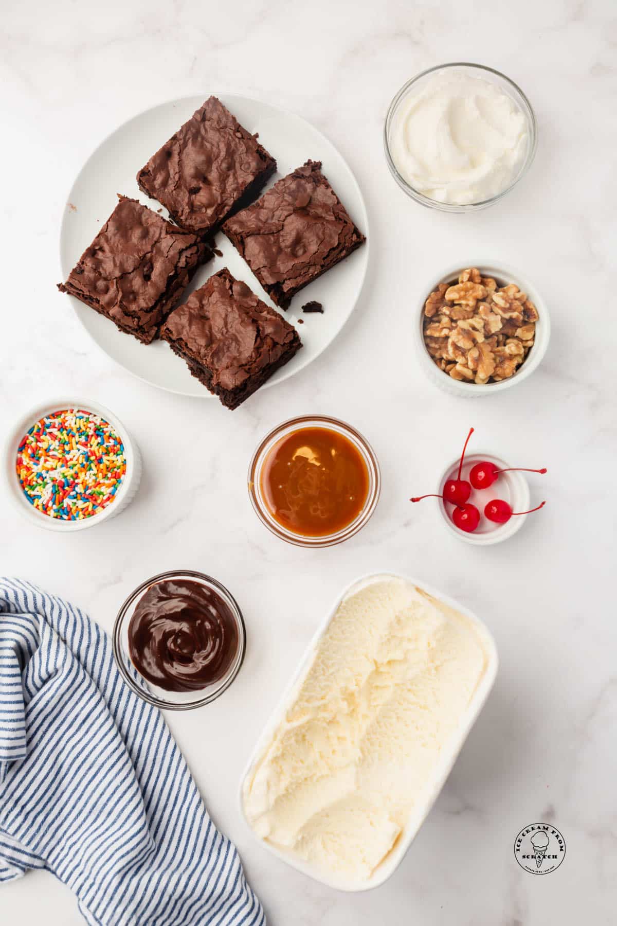 The ingredients to make a brownie a la mode sundae, all in small bowls around a plate of brownies.