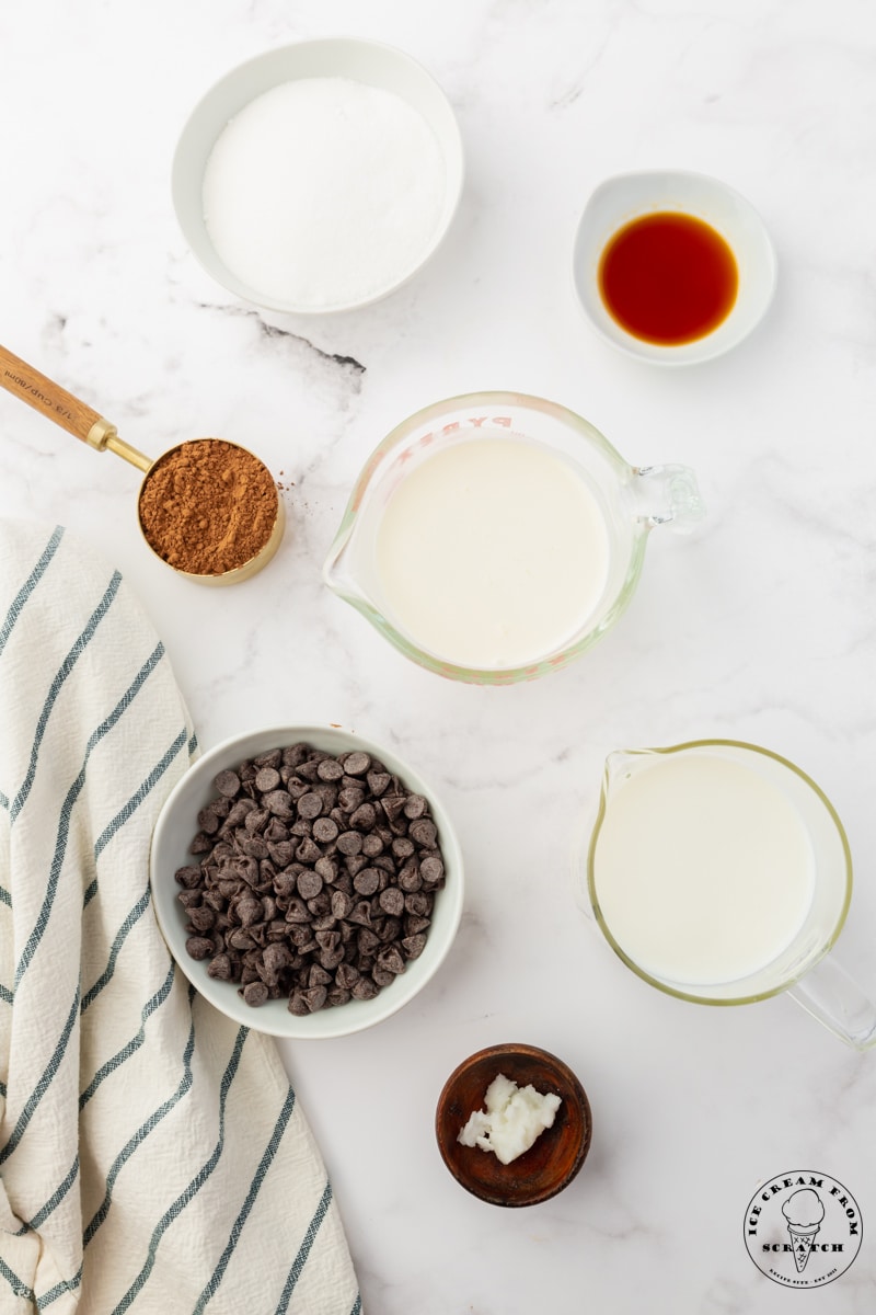 A bowl of chocolate chips, a bowl of milk, another of cream, and the rest of the ingredients needed to make chocolate ice cream bars.